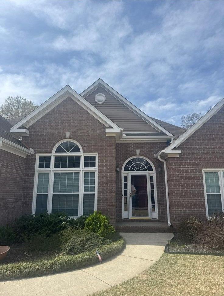 Brick house with arched windows and doorway, front porch, pathway, and cloudy sky.