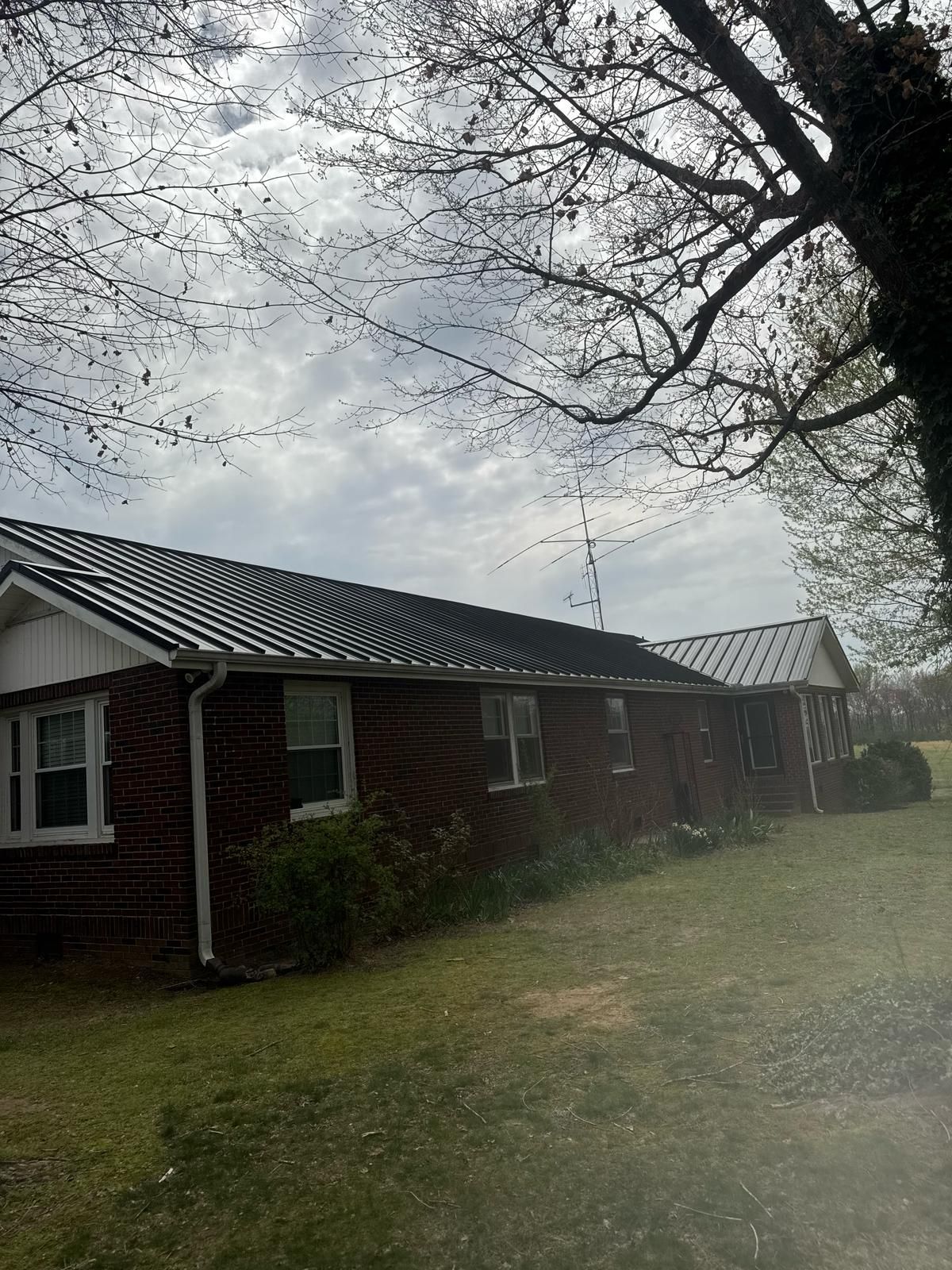 Brick house with black metal roof, white trim, and a cloudy sky.