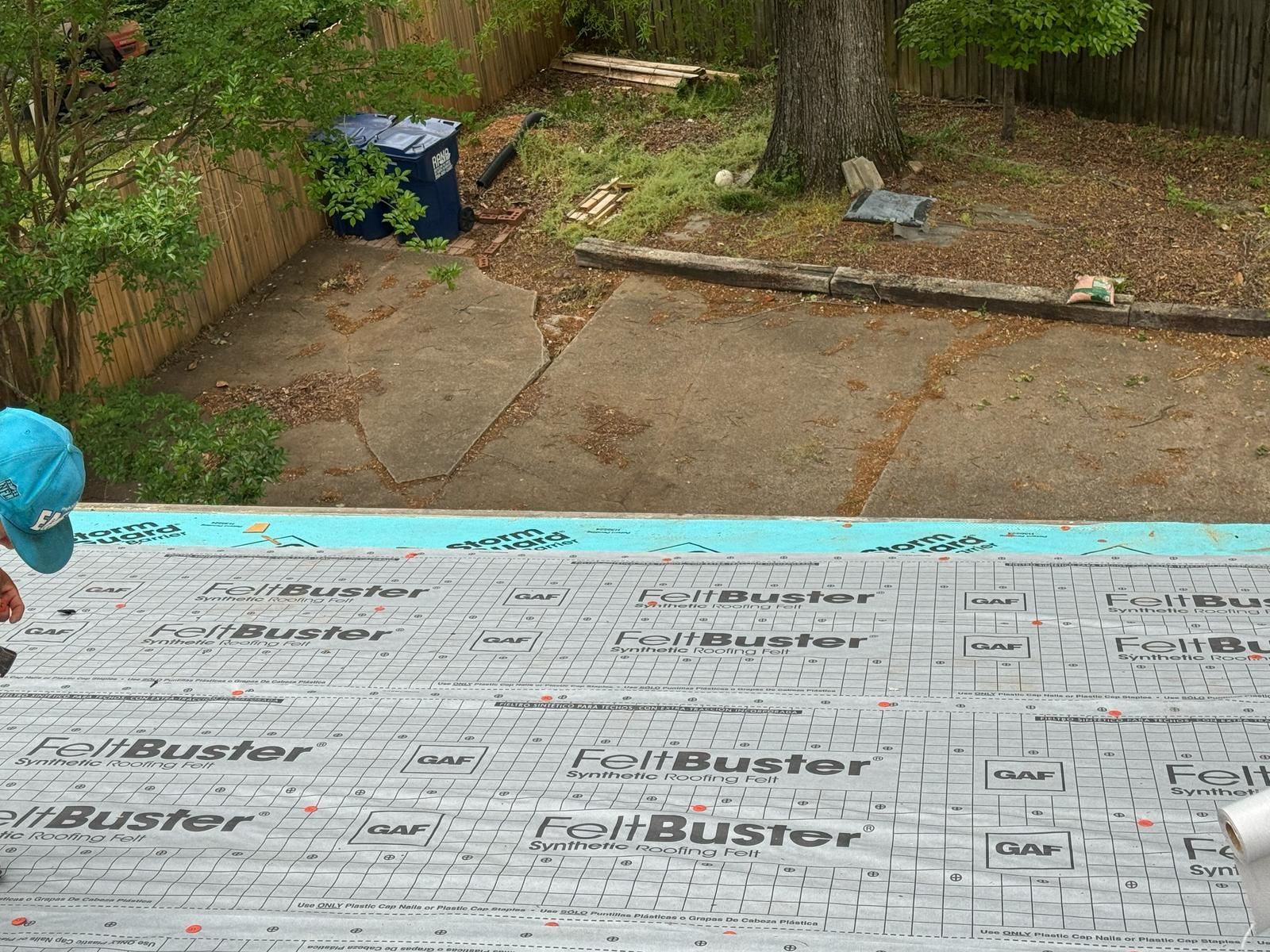 Person working on a roof, installing underlayment. Backyard in background.