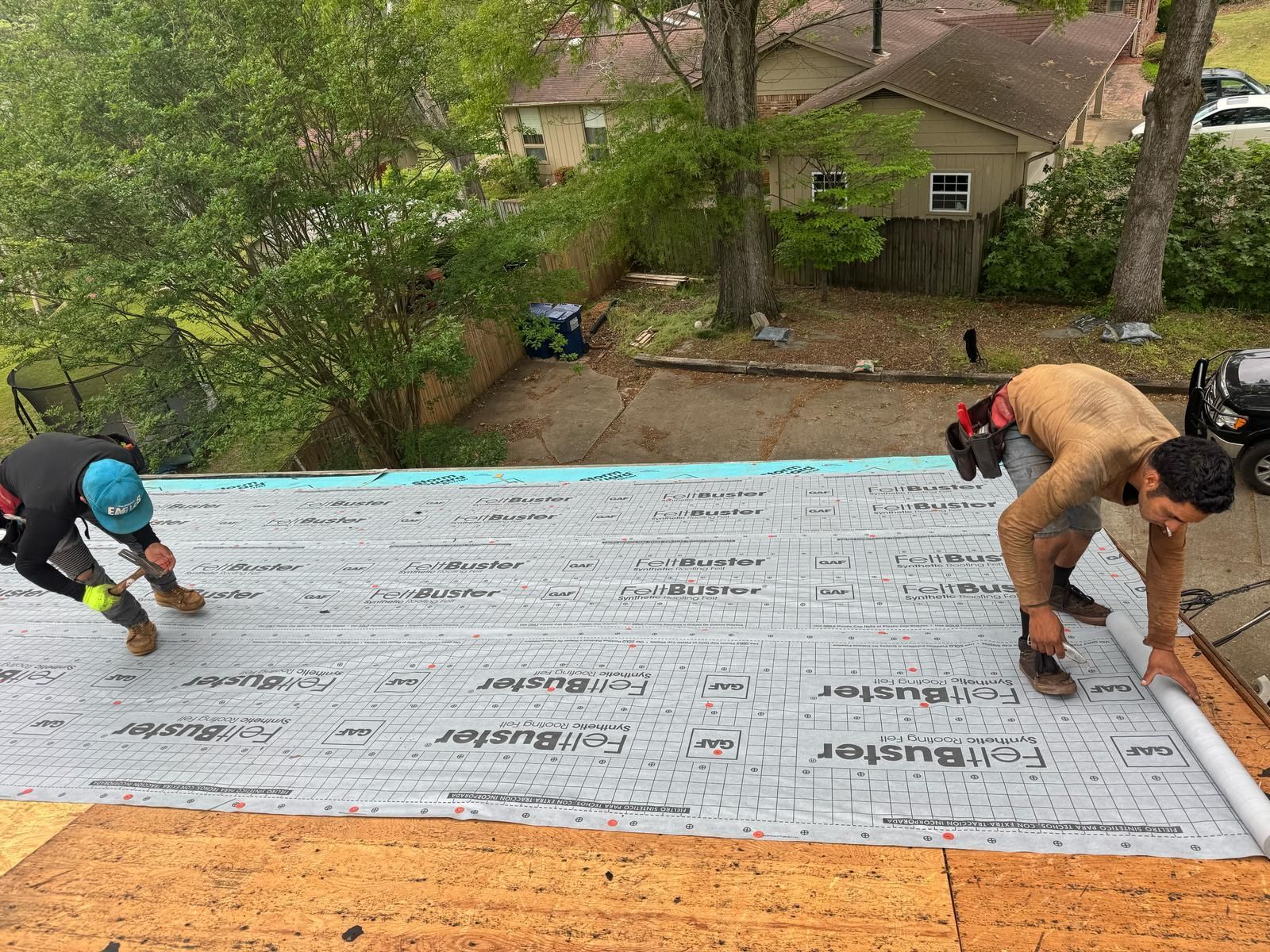 Two roofers installing roofing underlayment on a residential roof in a backyard setting.