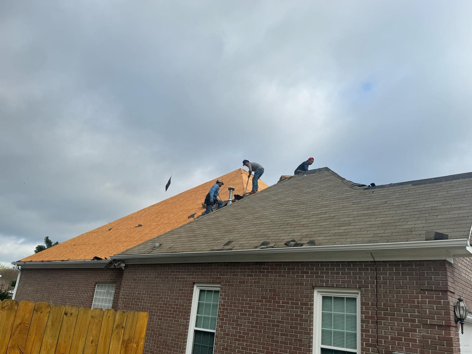 Roofers working on a house roof. One side is new, other is old. Overcast sky.