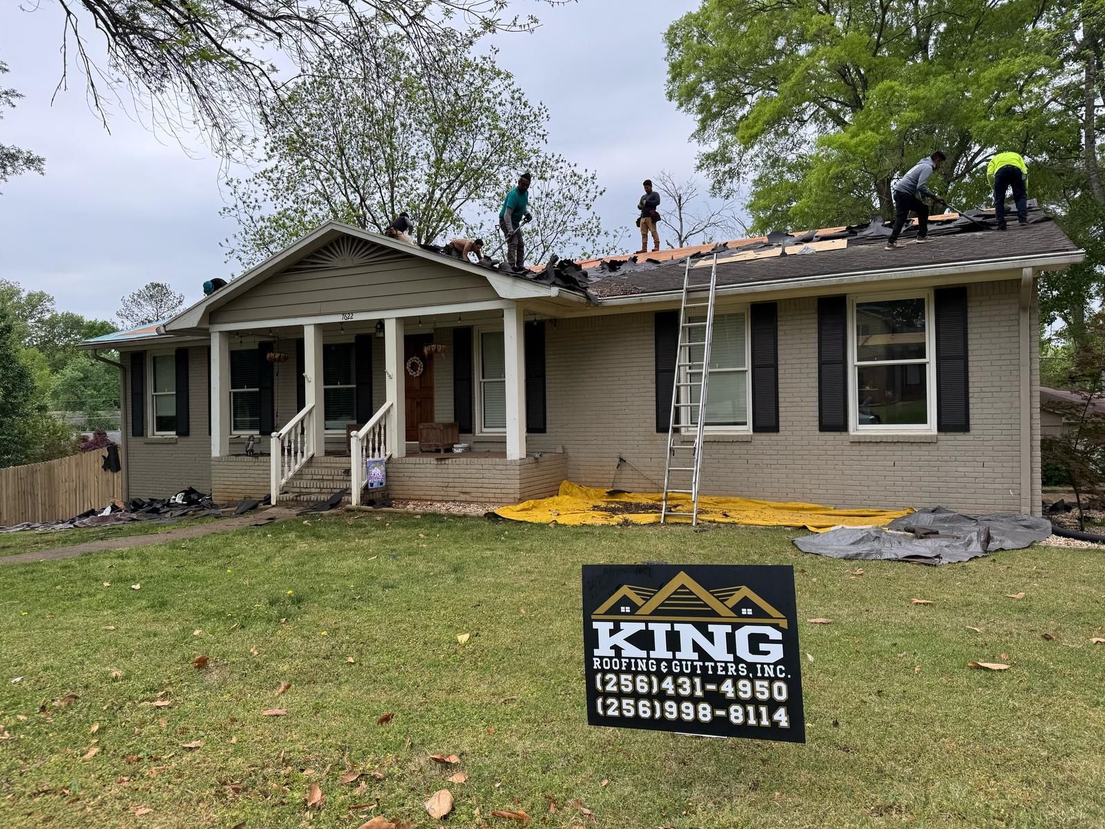 Roofing crew working on a house; removing old shingles. Sign in foreground.