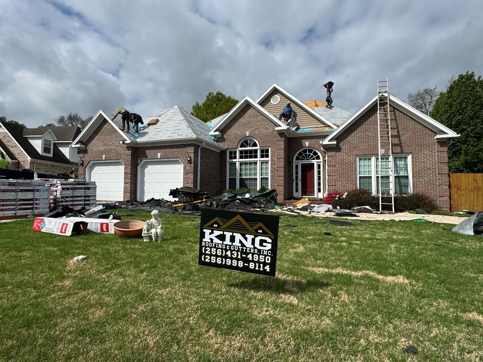 Roofing crew replacing shingles on a brick house under a cloudy sky.