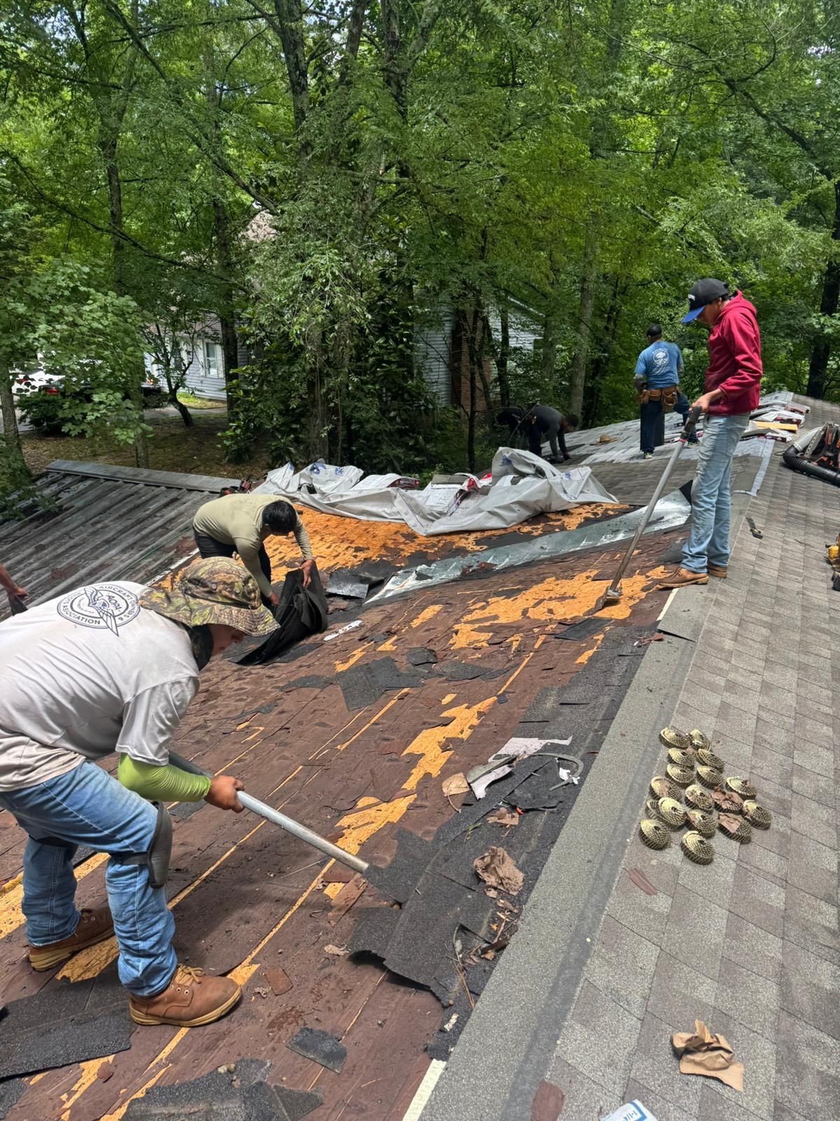 Roofers removing old shingles from a house roof on a sunny day.
