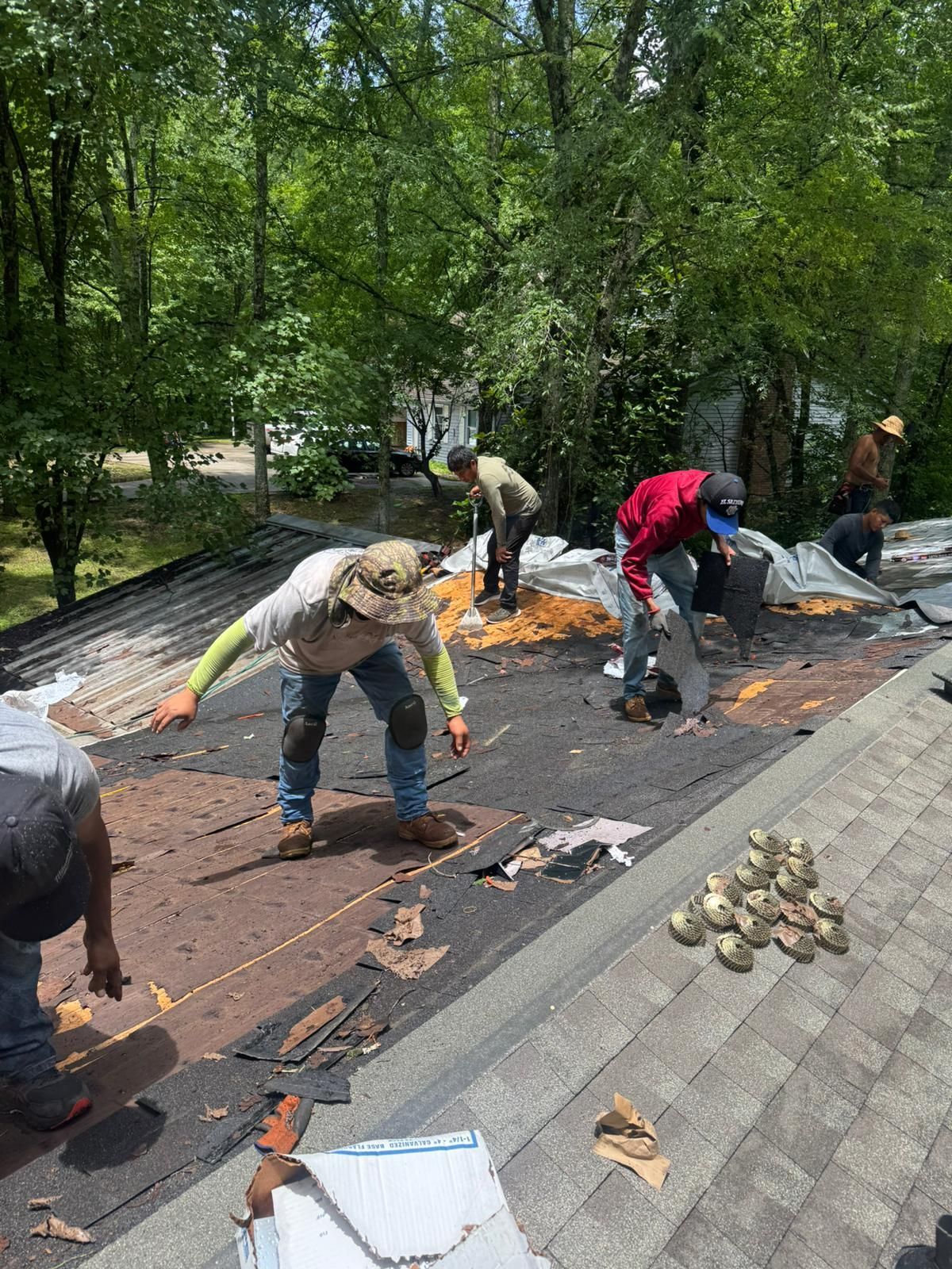 Roofing crew removes old shingles from a roof on a sunny day.