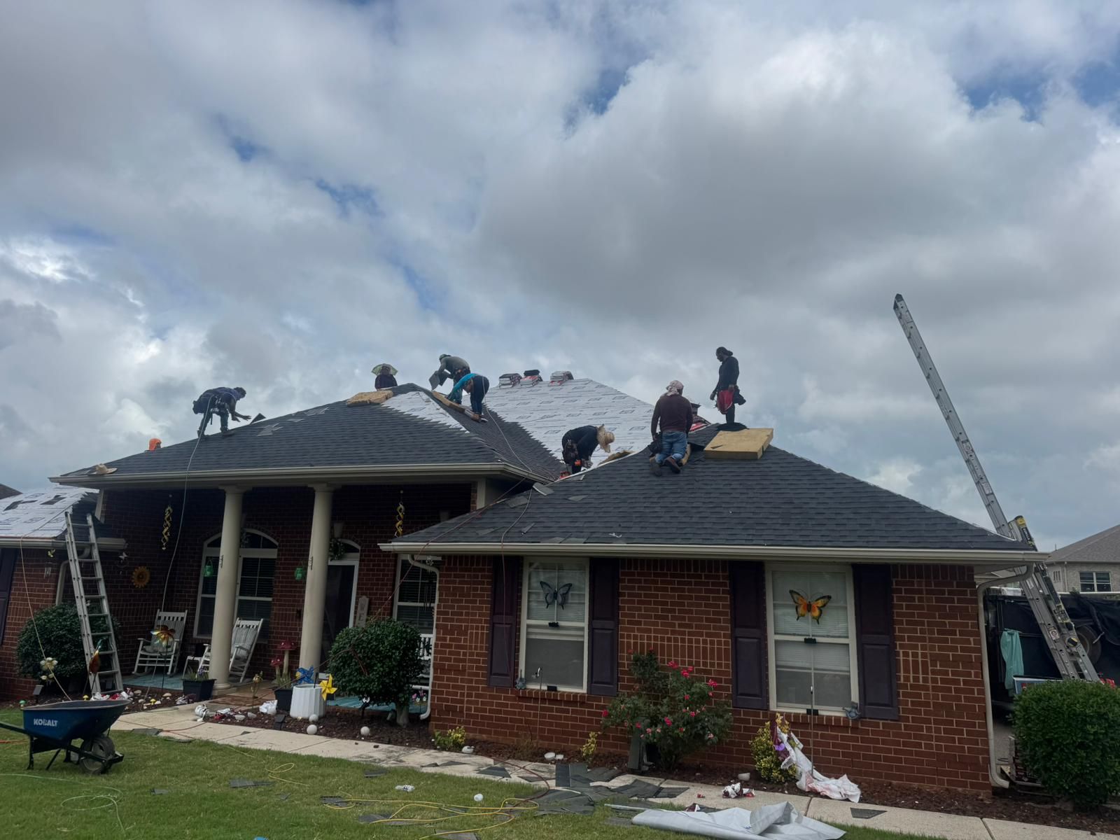 Roofers working on a residential home with ladders, cloudy sky overhead.