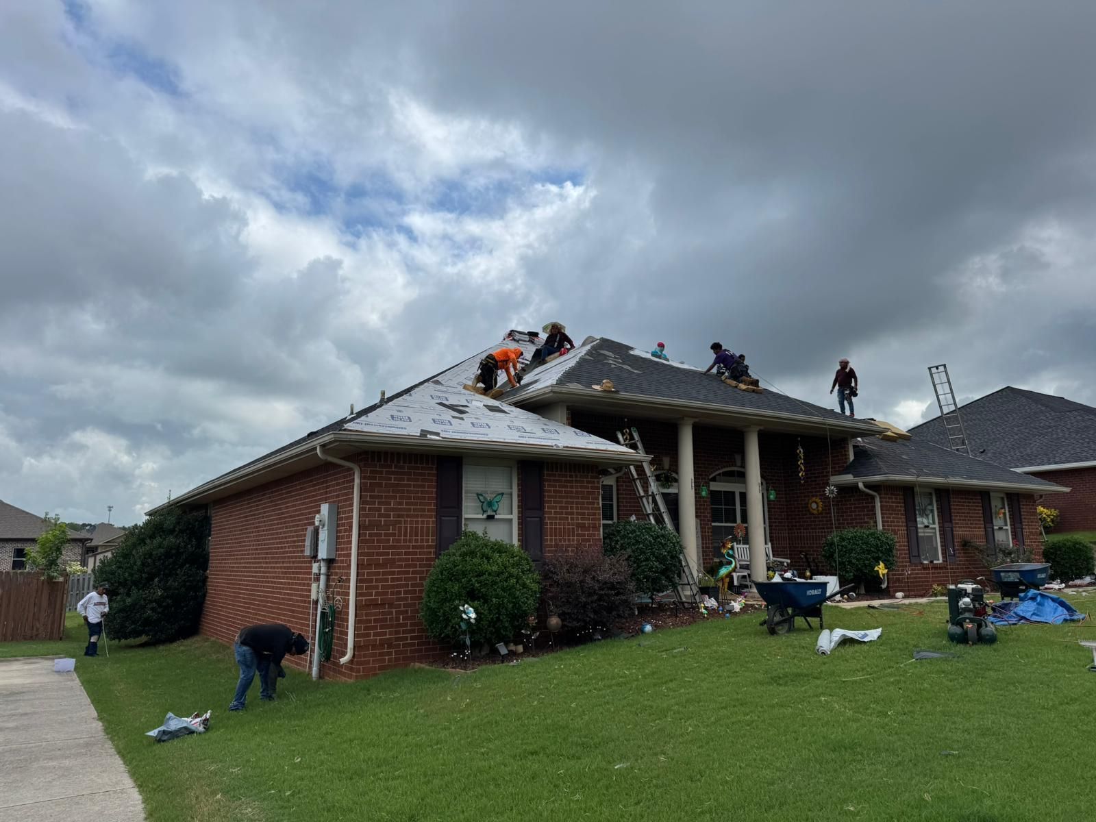 Workers replacing a roof on a brick house under a cloudy sky.