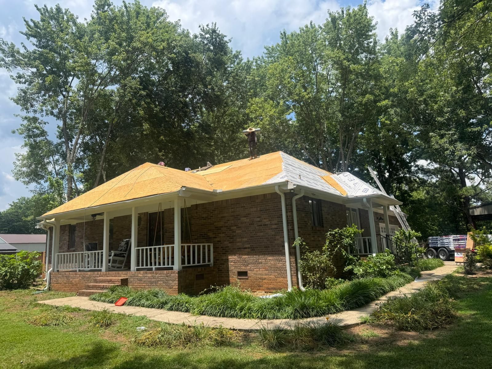 Brick house with a partially exposed roof and trees in the background.