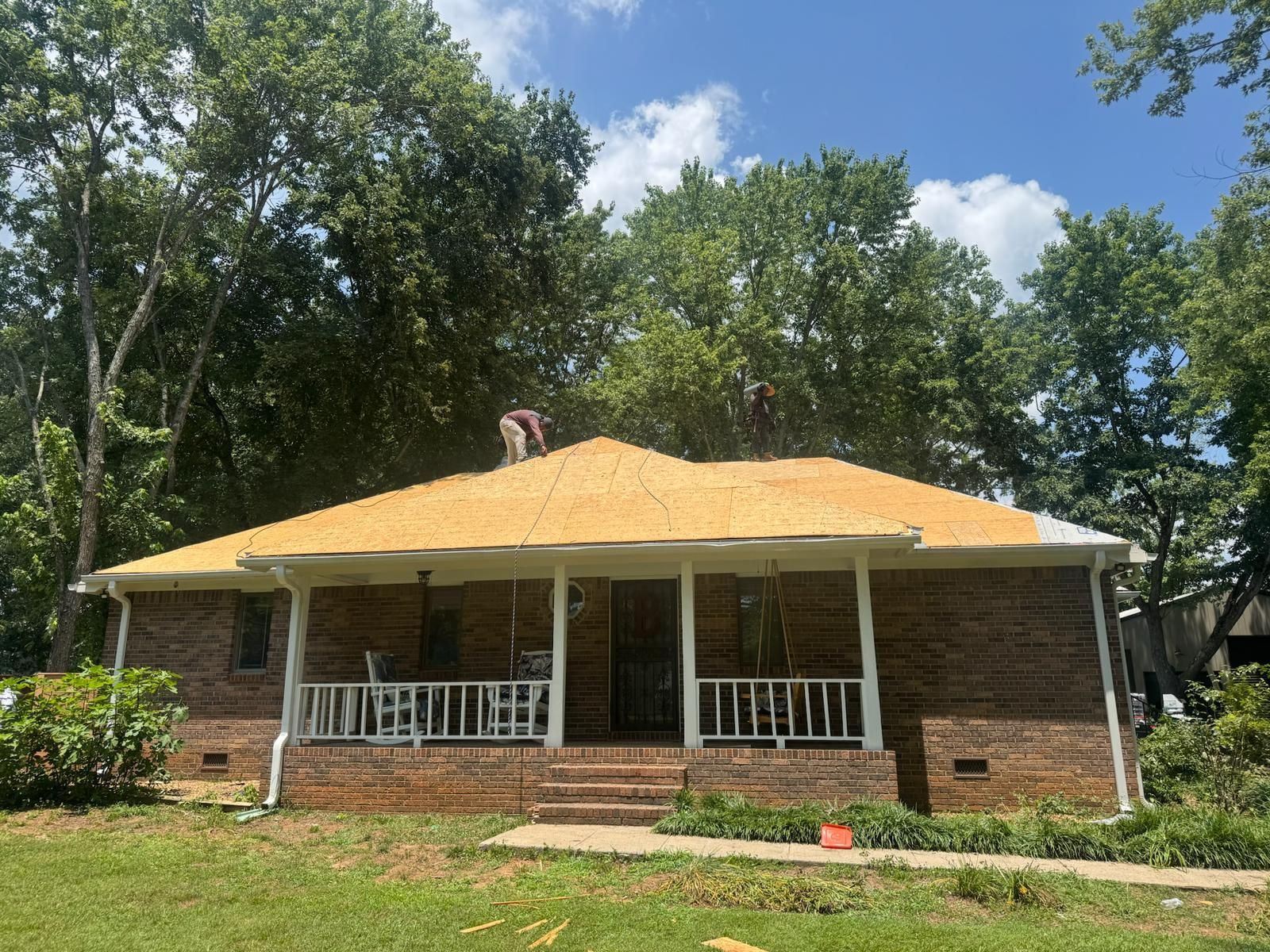 Home with roofing work in progress; tan roof, brick exterior, white porch. Person on roof.