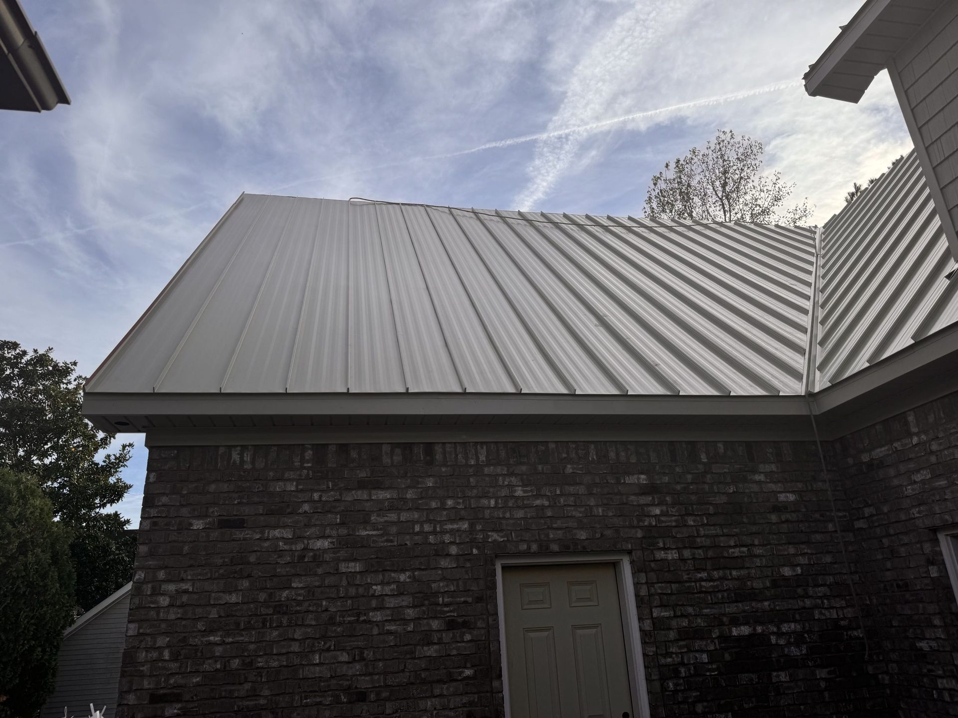 Brick building with a gray metal roof under a cloudy sky.