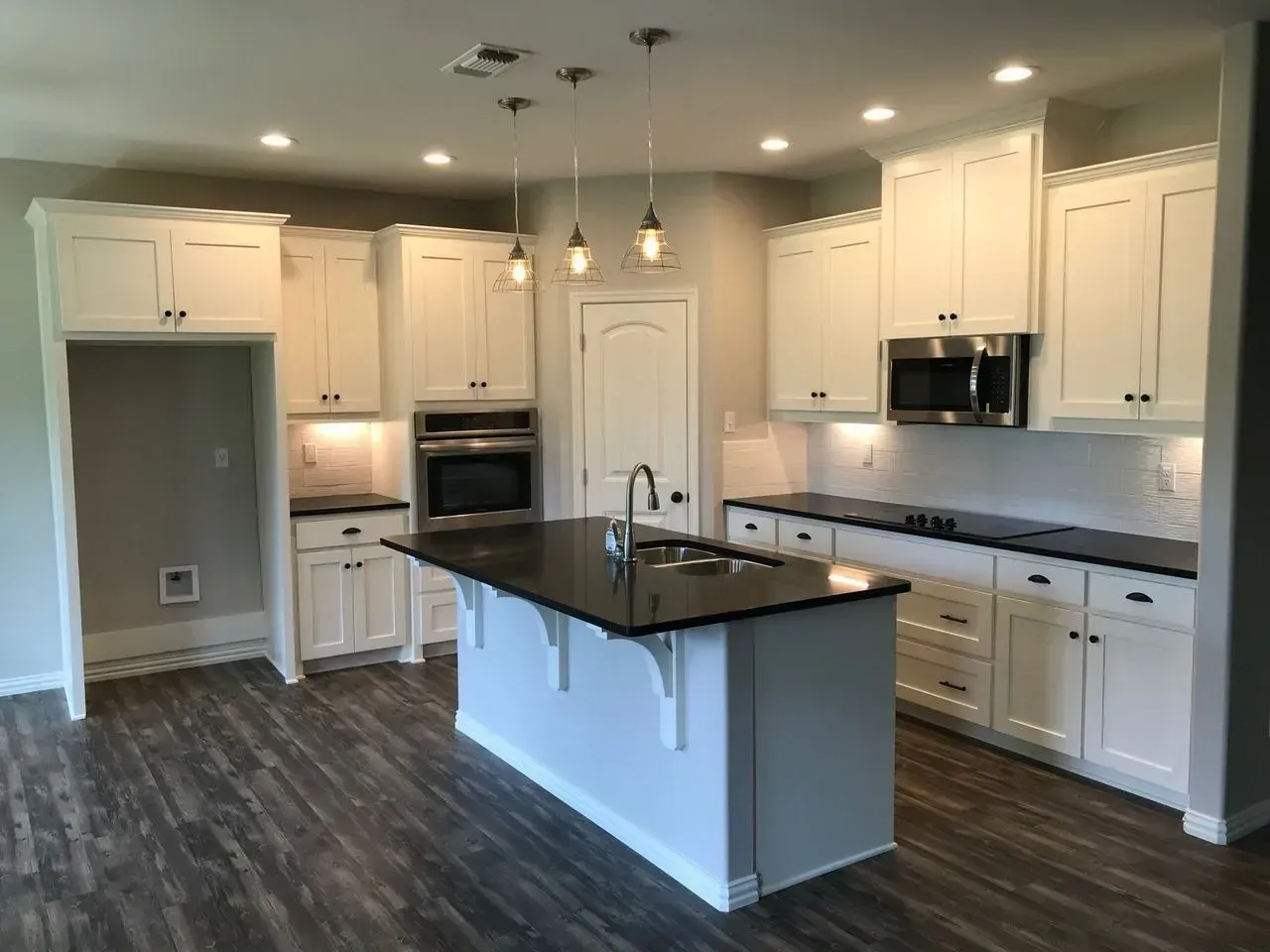 A kitchen with white cabinets , black counter tops , and stainless steel appliances.