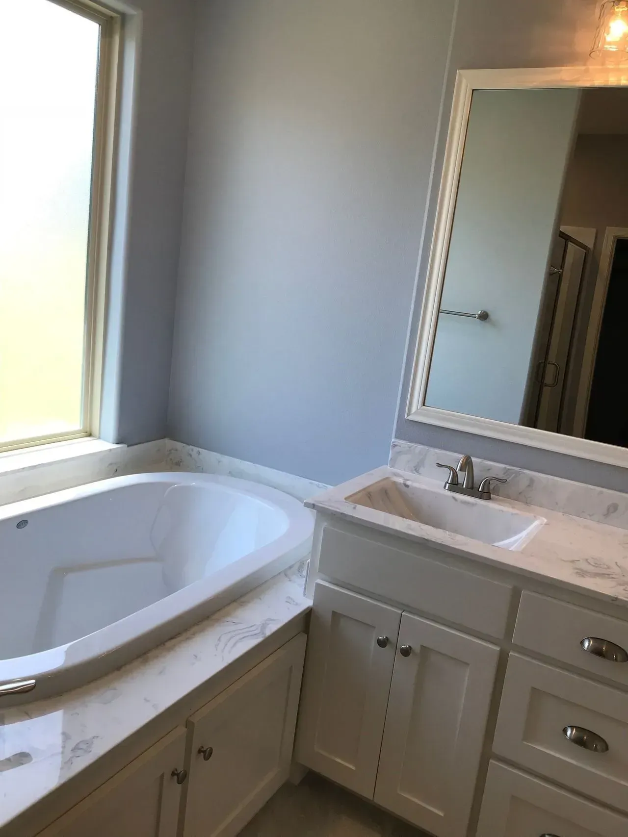 A bathroom with a tub , sink , mirror and window.