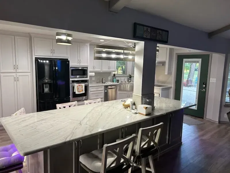 A kitchen with a large island , stools and a refrigerator.