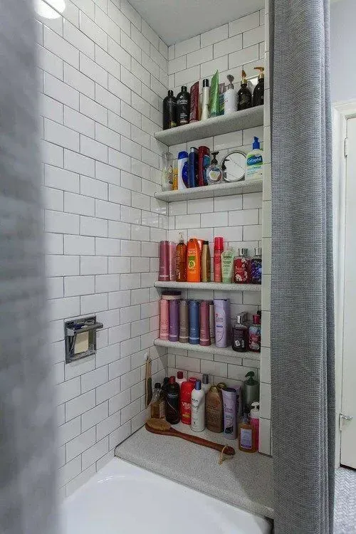 A bathroom with white brick walls and shelves filled with bottles of shampoo and conditioner.