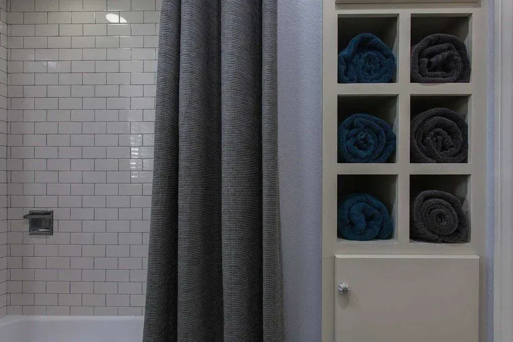 A bathroom with a shower curtain and a shelf filled with towels.