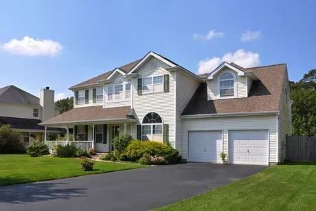 A large white house with a brown roof and two garage doors