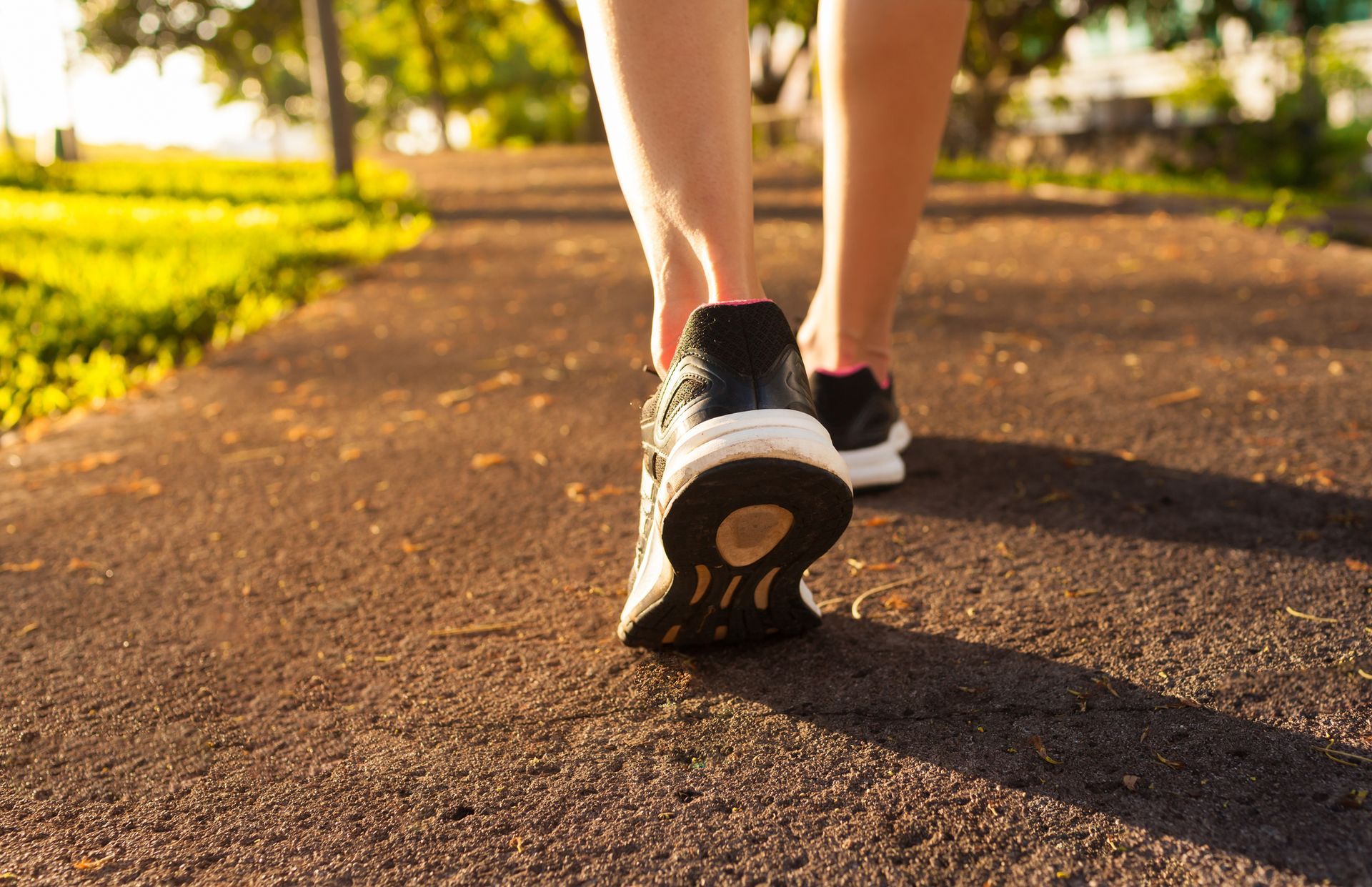 Person walking on a paved path, wearing black and white sneakers, sunny outdoor setting.