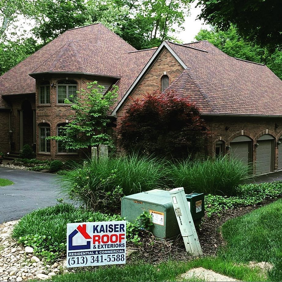 A large brick house with a kaiser roof company sign in front of it