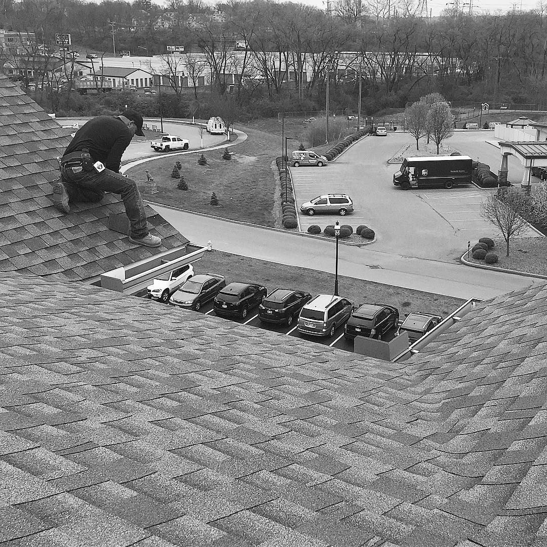 A black and white photo of a man sitting on top of a roof.