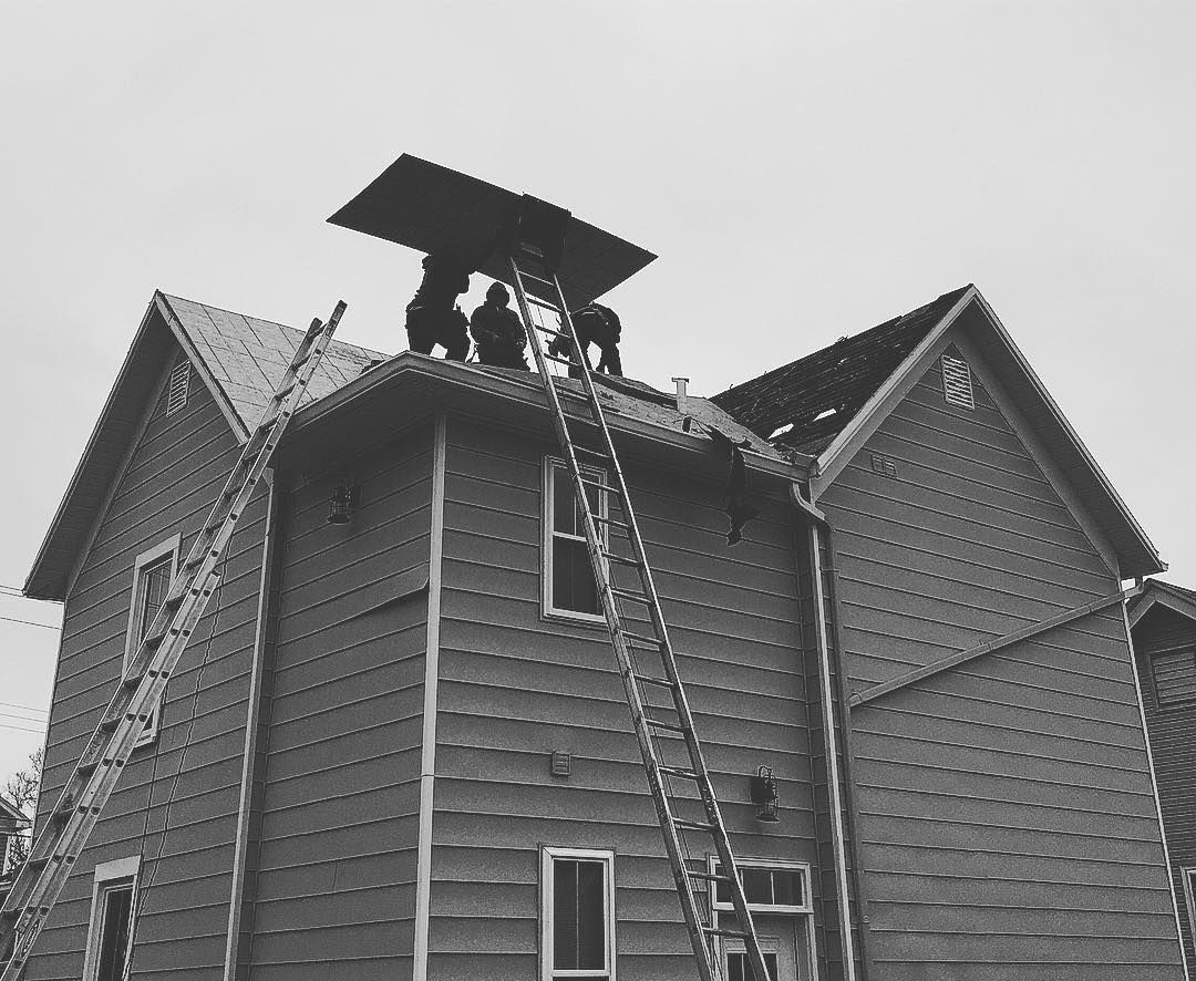 A black and white photo of a house with people on the roof