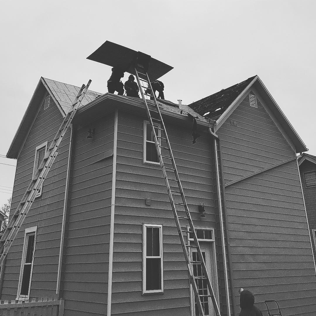 A black and white photo of people working on the roof of a house