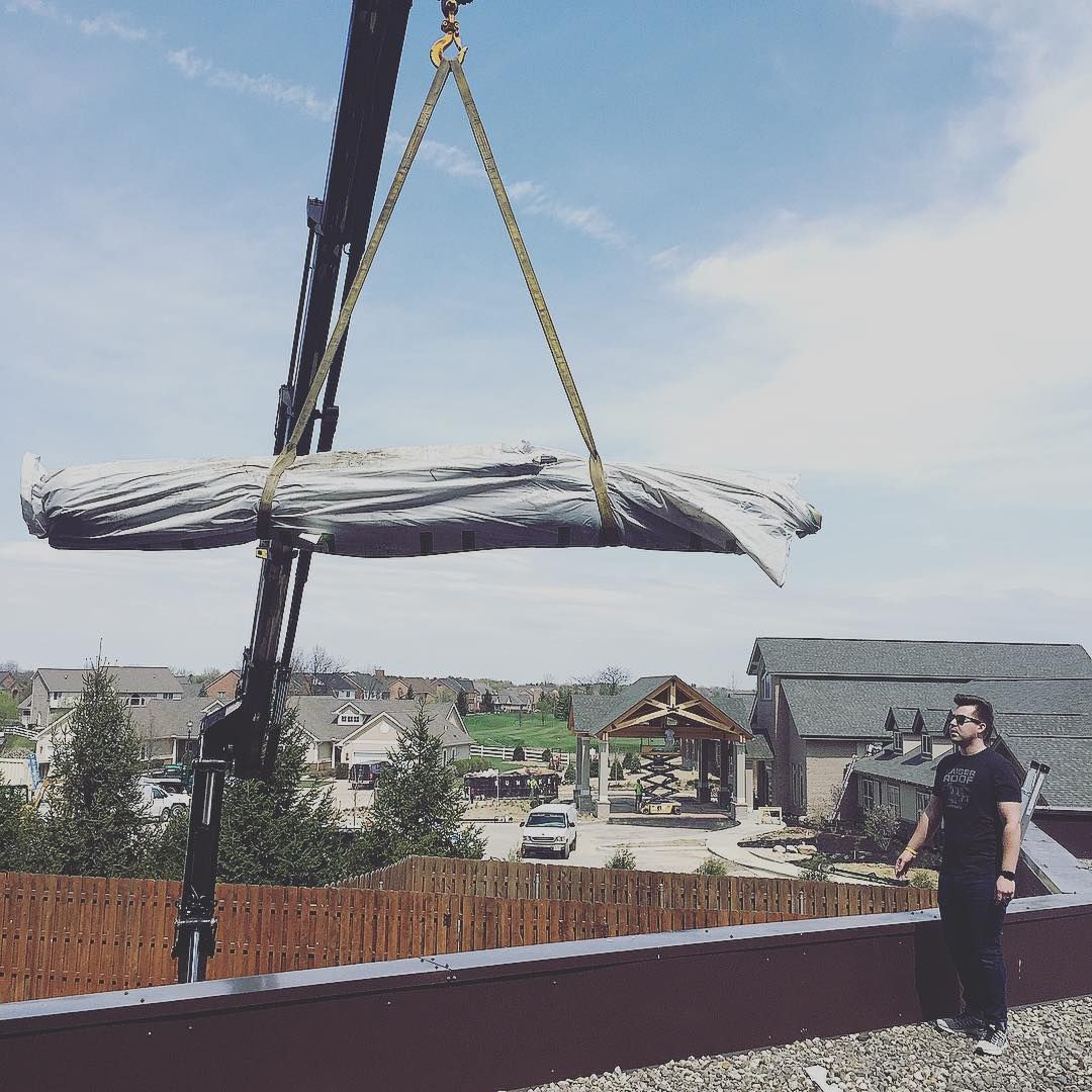 A man is standing on a roof watching a large piece of wood being lifted by a crane.