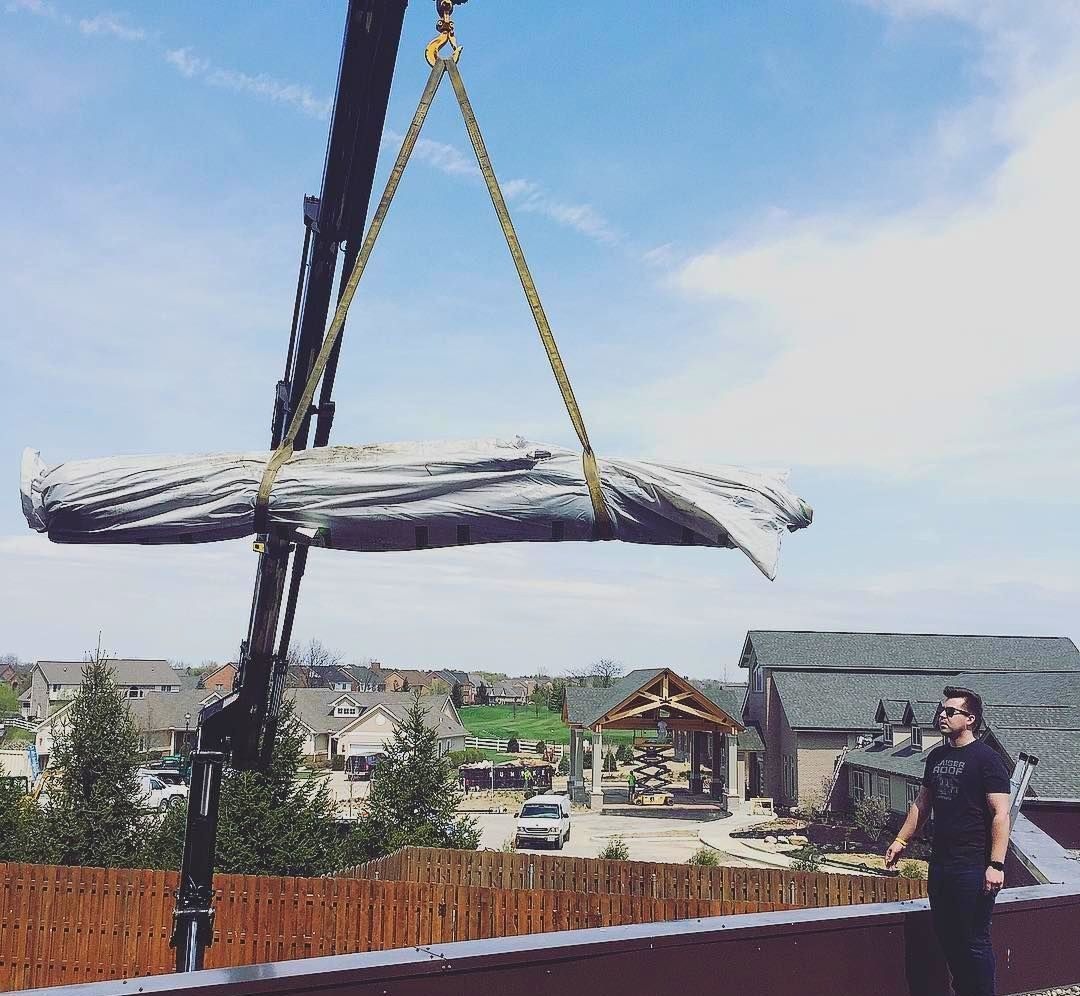 A man is standing on a roof watching a large log being lifted by a crane.