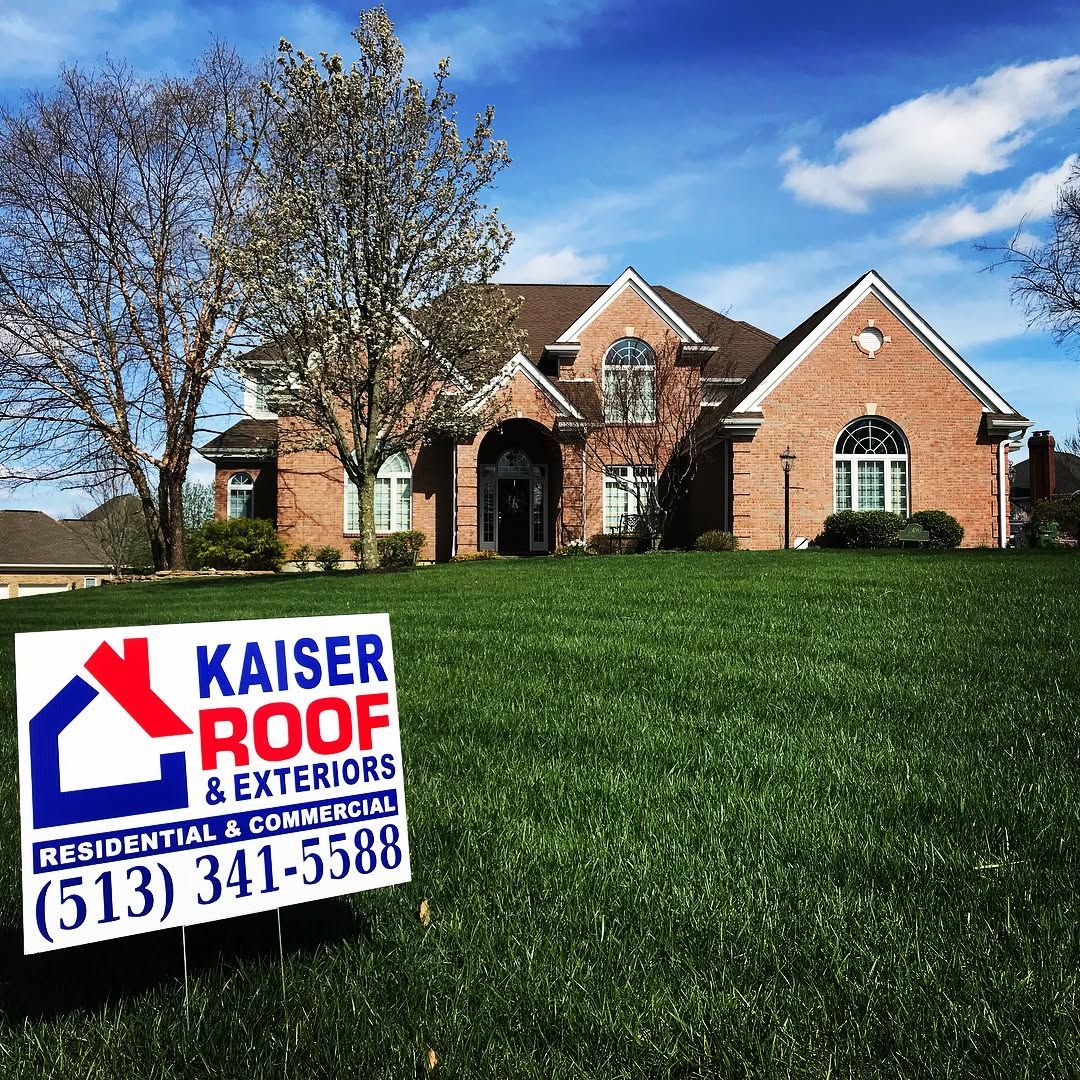 A kaiser roof and exteriors sign is in front of a large brick house.