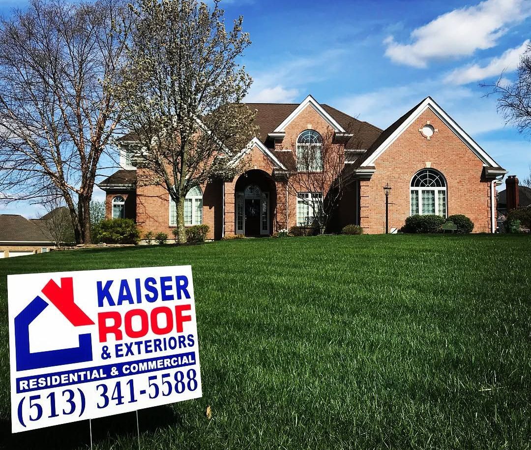 A large brick house with a kaiser roof and exteriors sign in front of it
