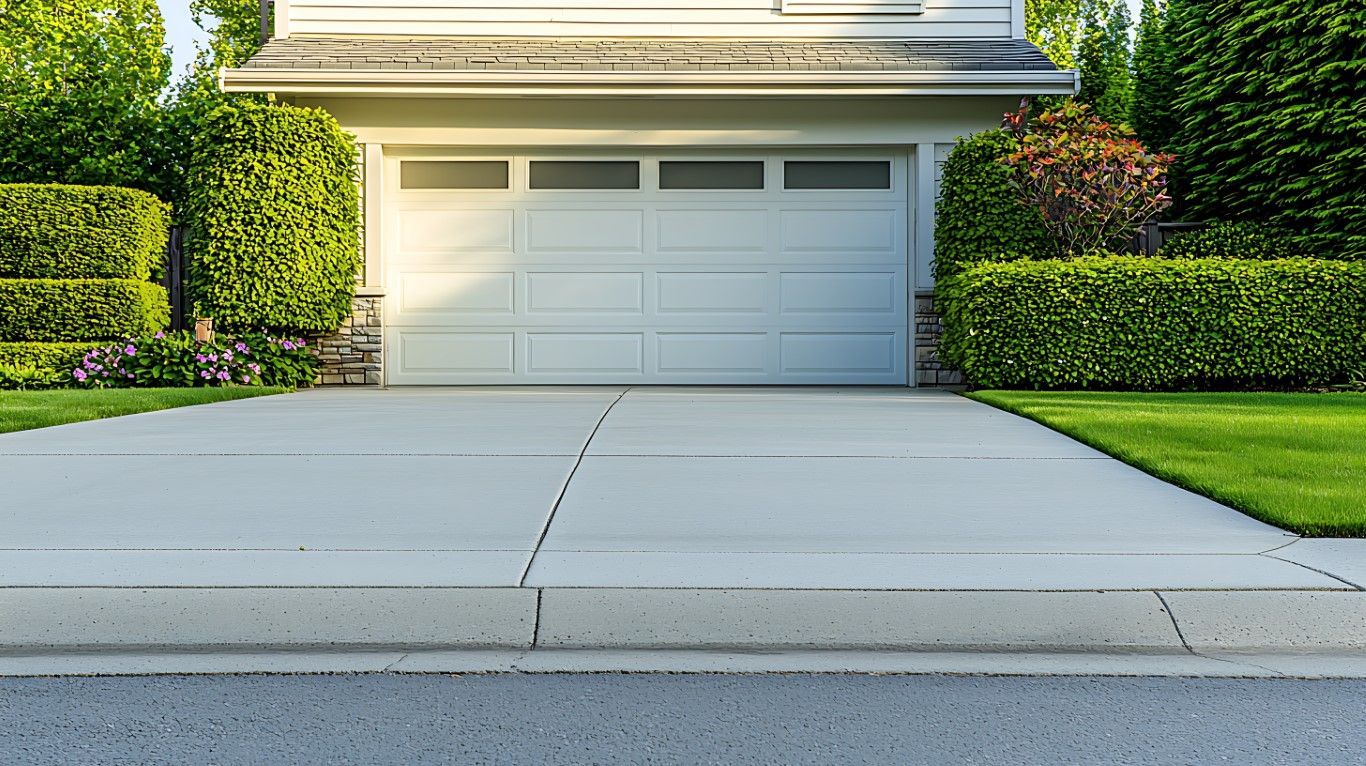 A white house with a white garage door and a concrete driveway leading to it.
