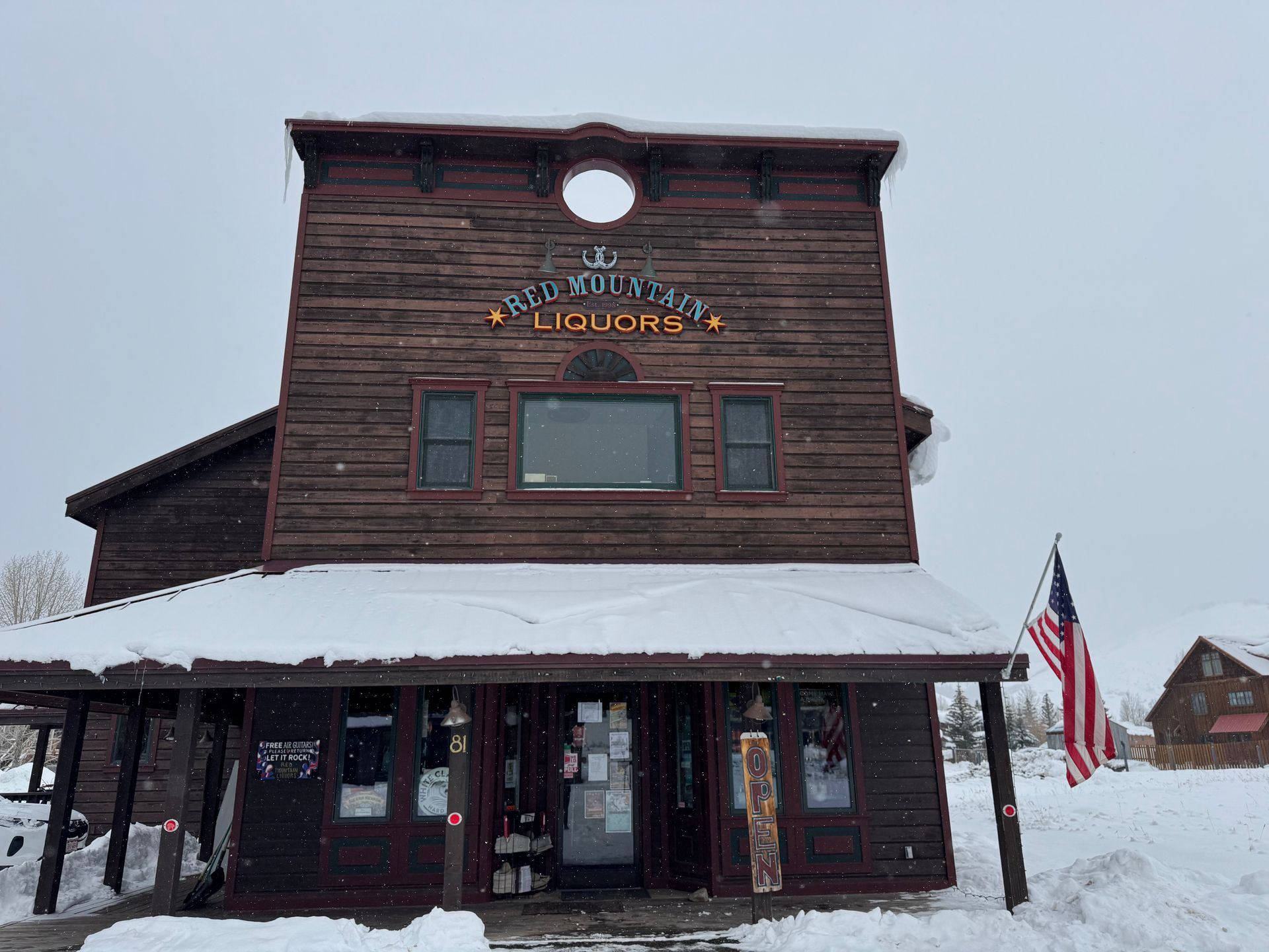 A large wooden building covered in snow with an american flag in front of it.