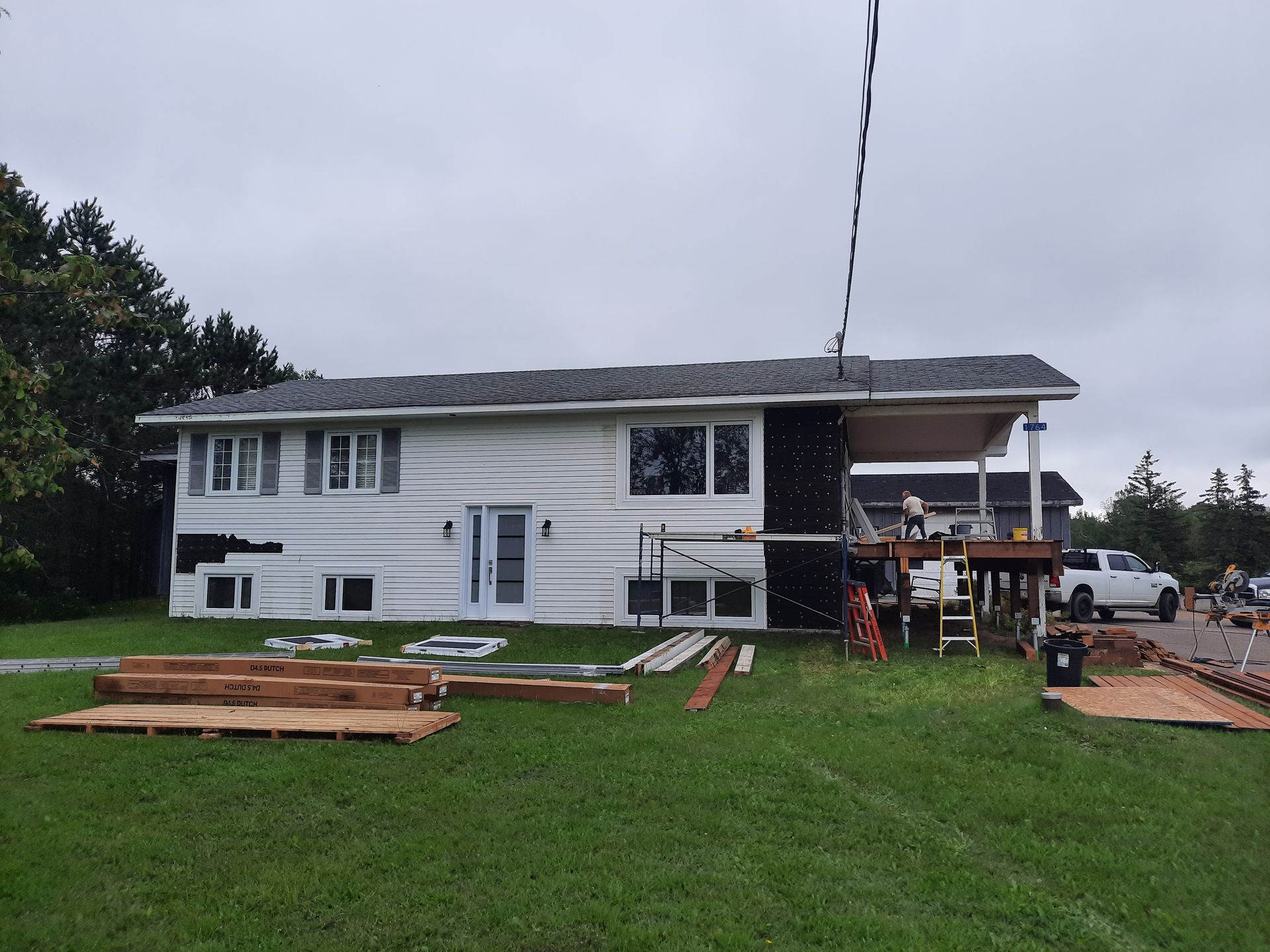 A large white house with a porch and a lot of wood in front of it.