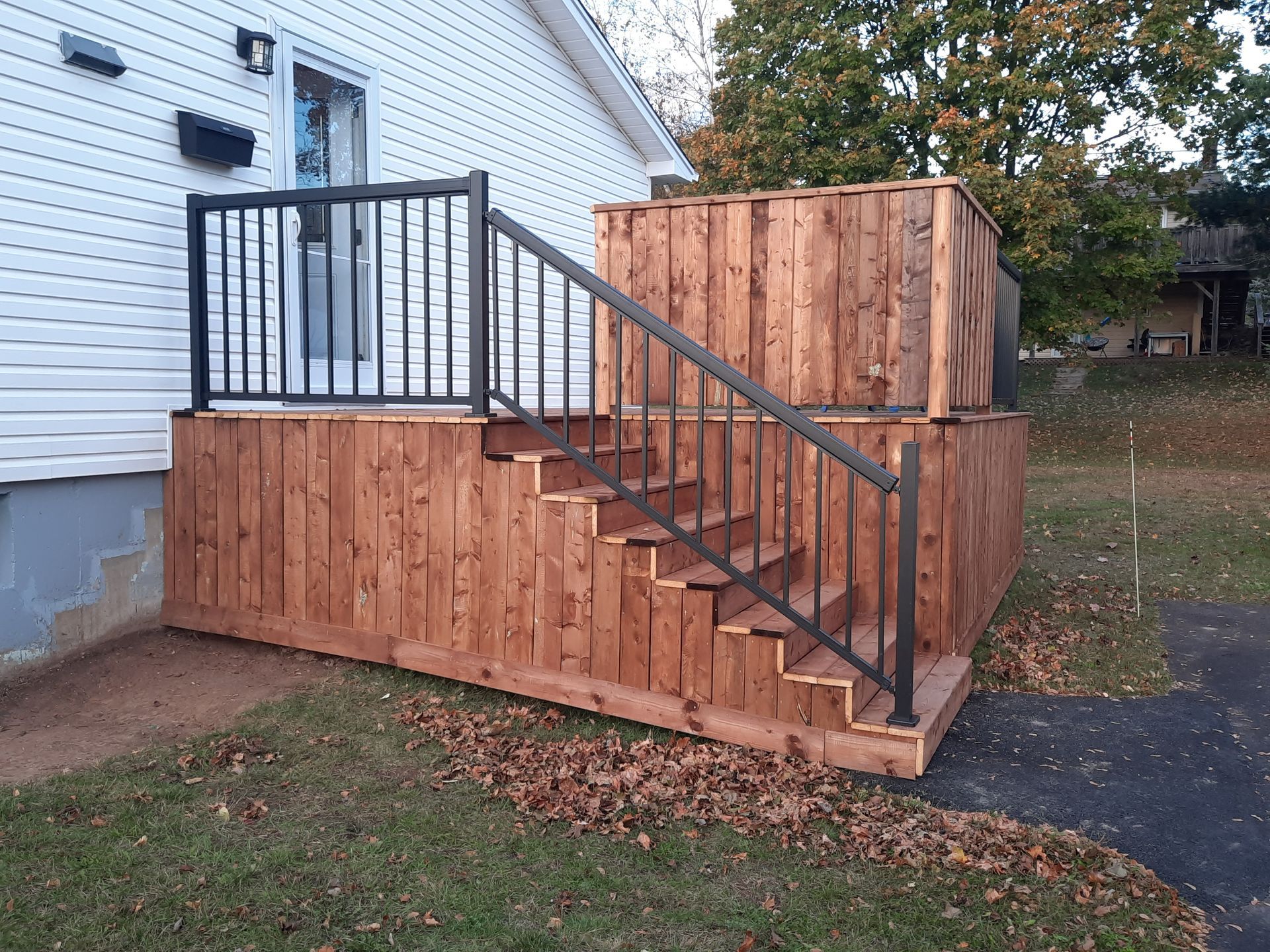 A wooden deck with stairs and a metal railing is in front of a house.