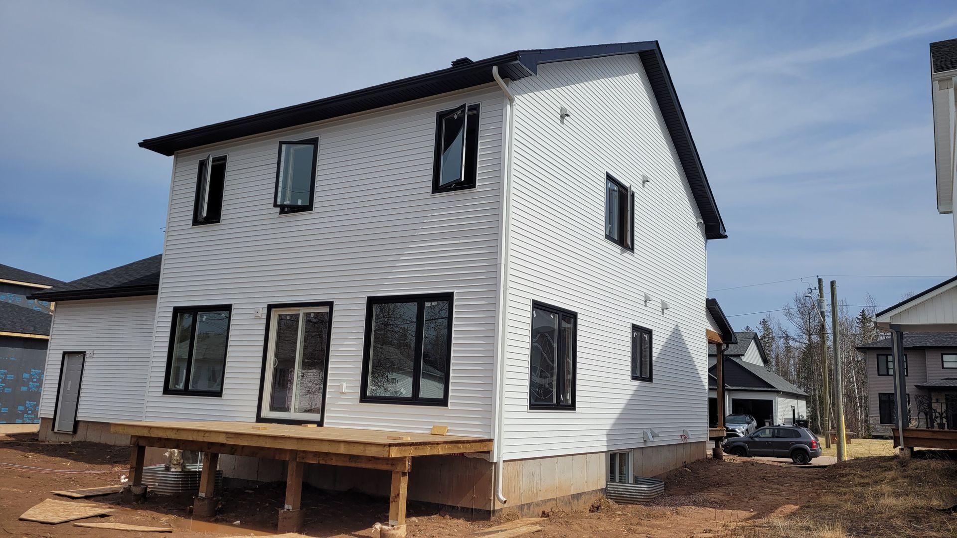 A white house with black windows is being built in a residential area.