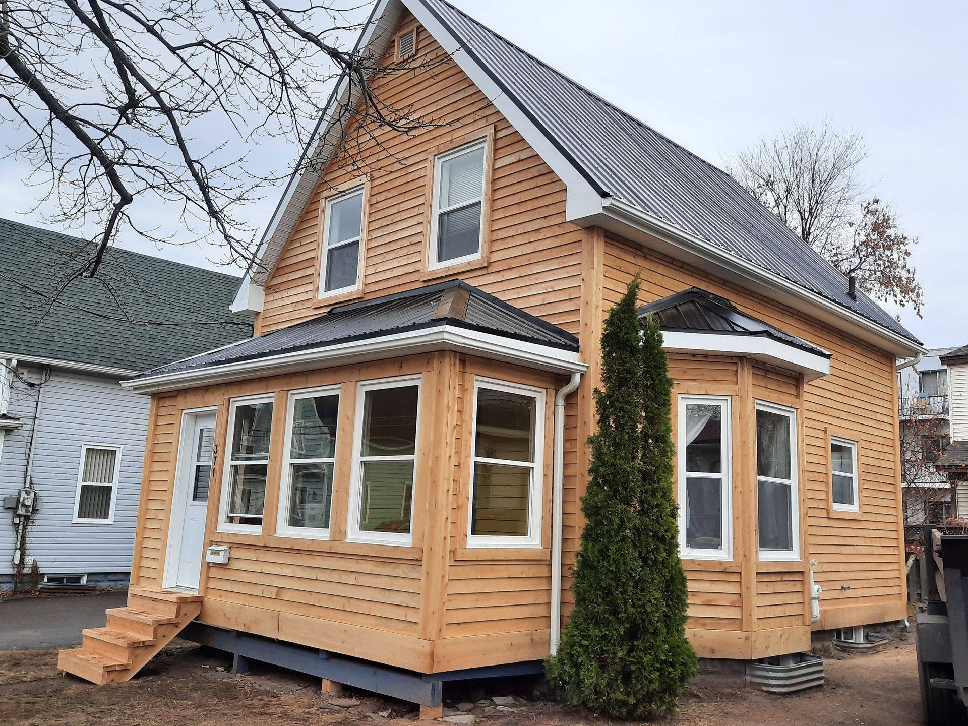 A small wooden house with a gray roof is sitting next to a white house.