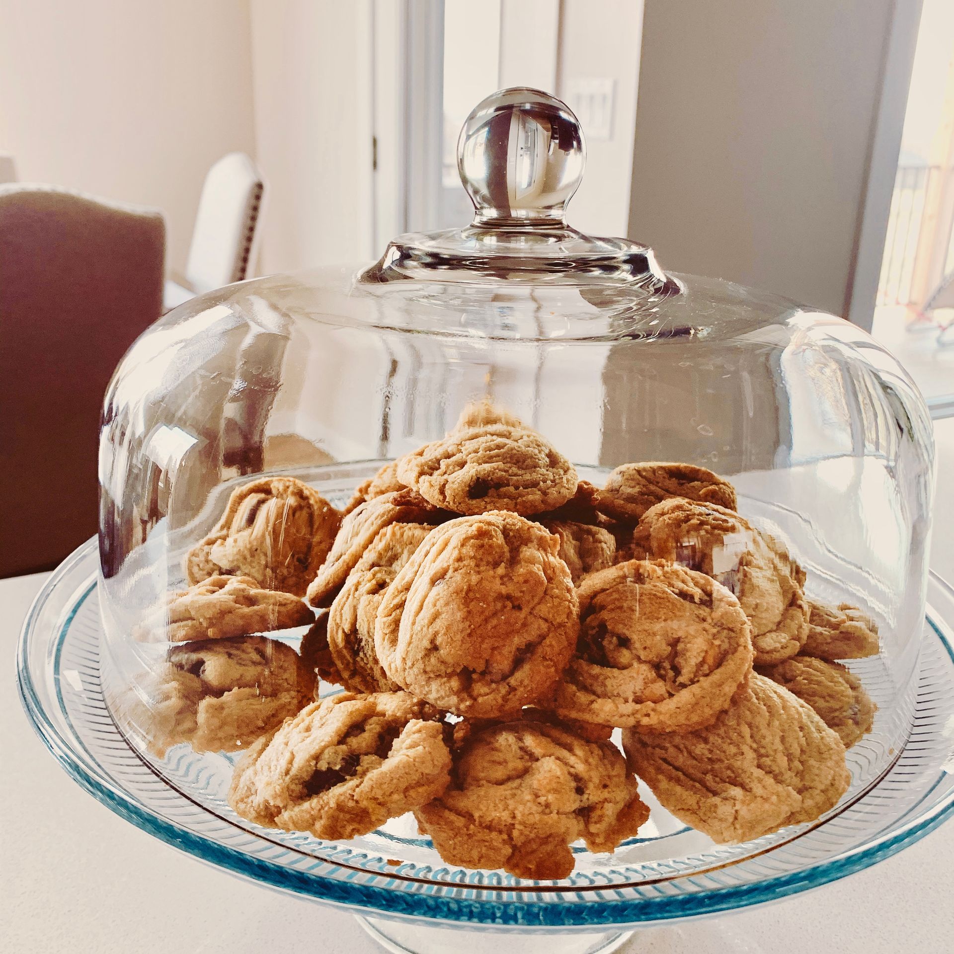 A glass plate filled with chocolate chip cookies under a glass dome.