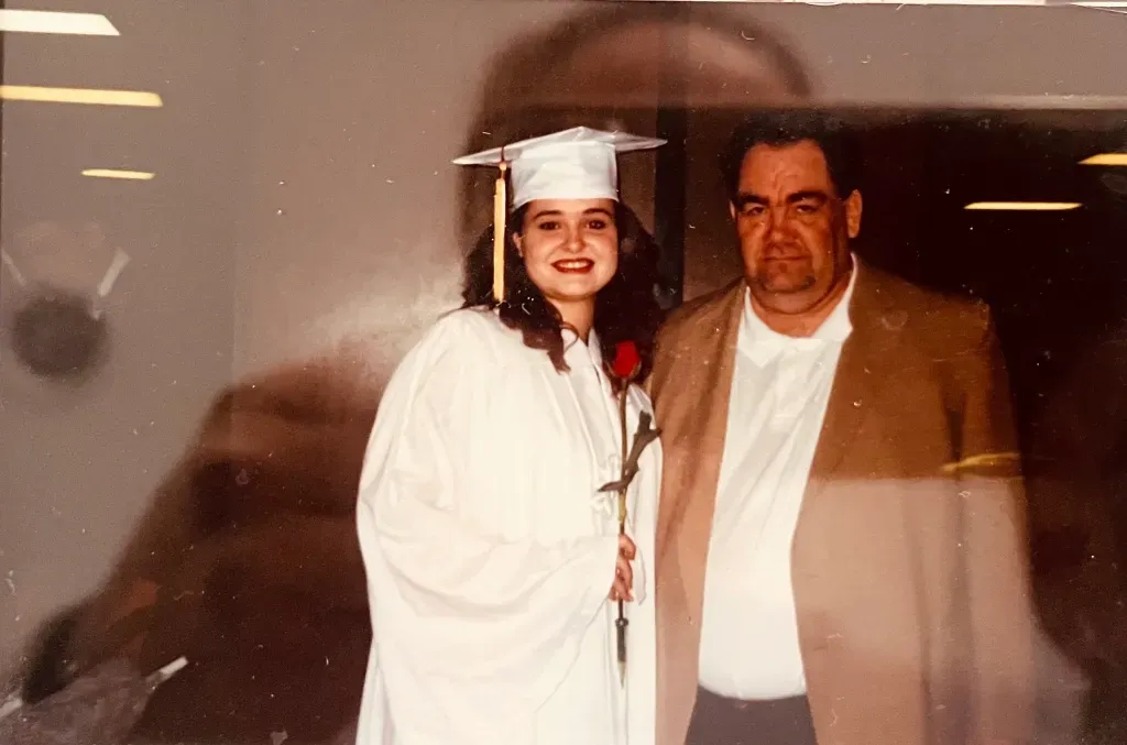 A woman in a graduation cap and gown is standing next to a man in a suit.