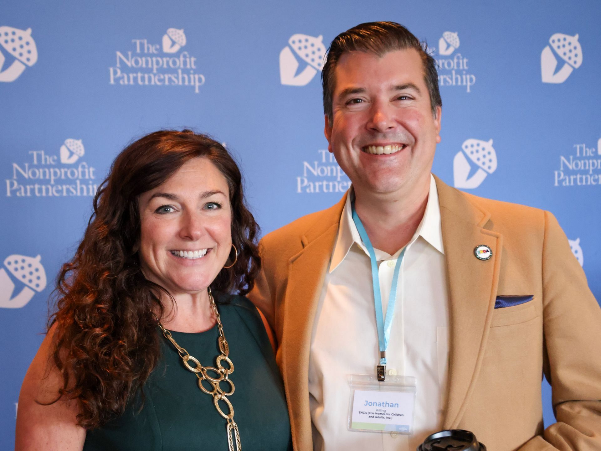 Two smiling people pose for a photo in front of a blue background with 