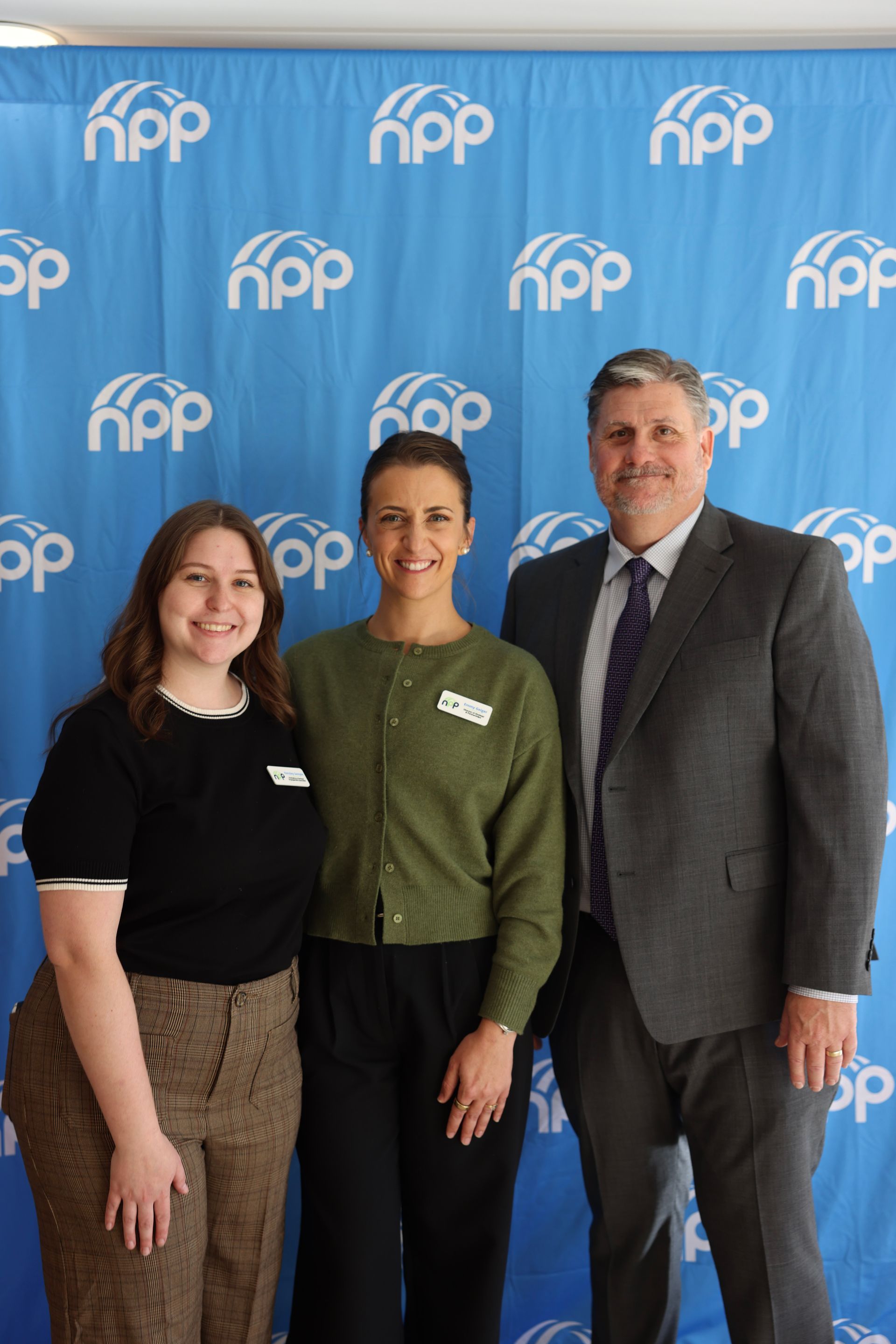 Three people stand smiling in front of a blue backdrop with a repeating
