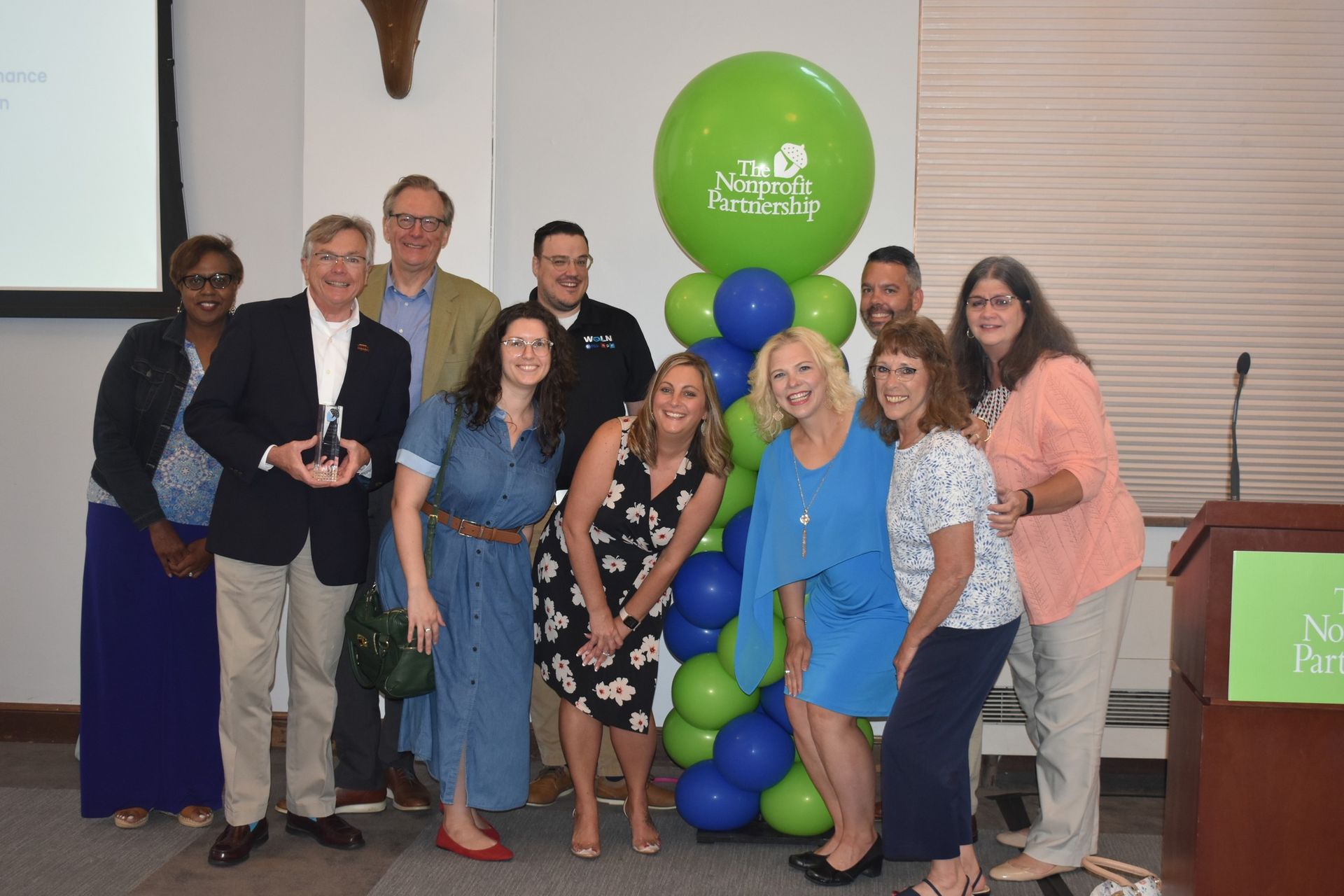 A group of twelve people smiling and posing in front of a balloon pillar with a 