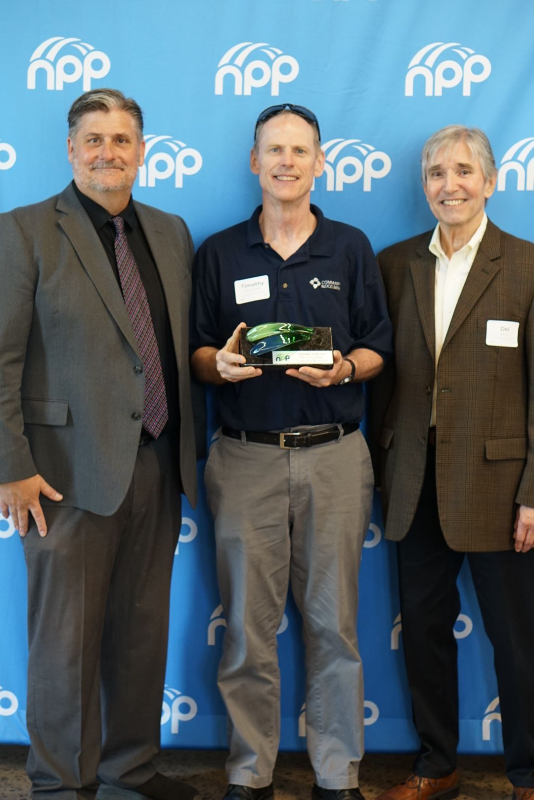 Three men stand before a blue background branded with 