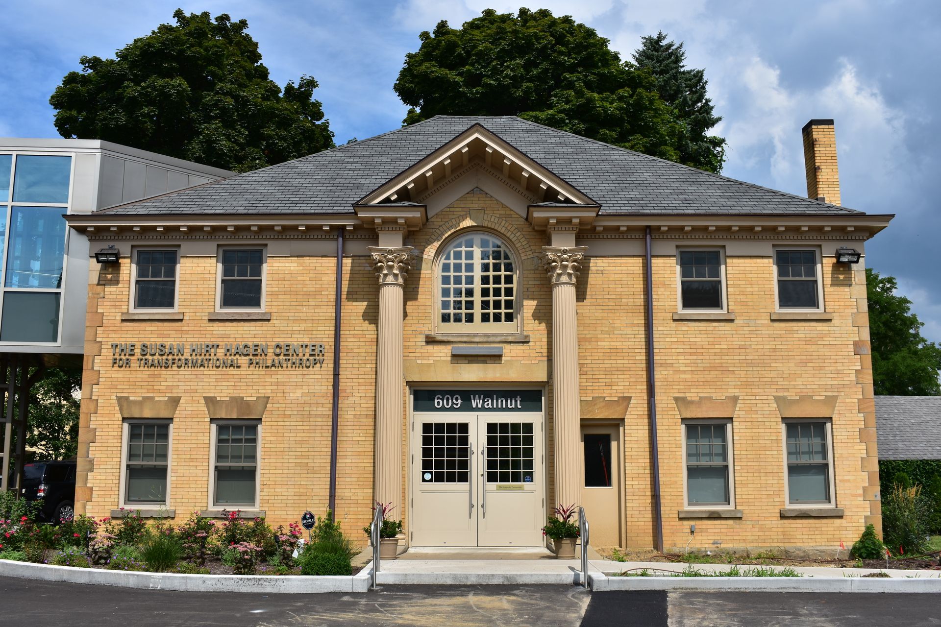 A symmetrical, two-story stone building with a central entrance, dual columns, an arched window, and a gray shingled roof.