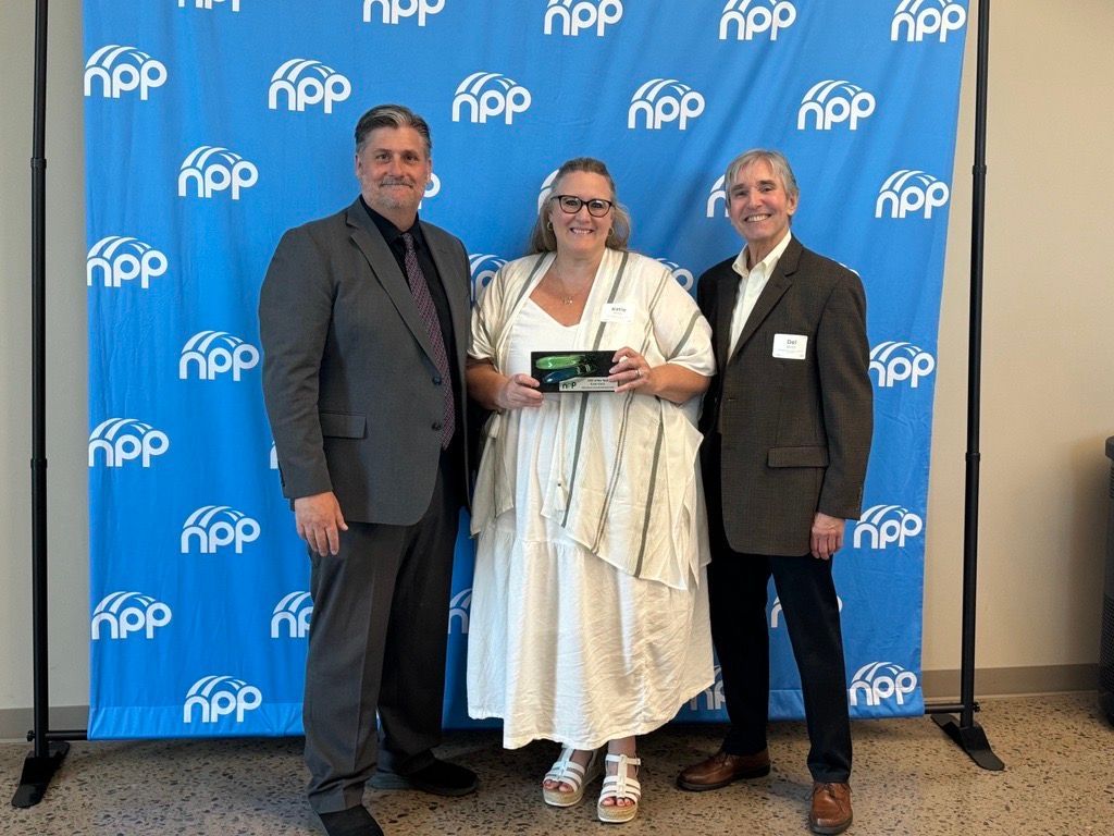Three people stand smiling in front of a blue backdrop with repeating 