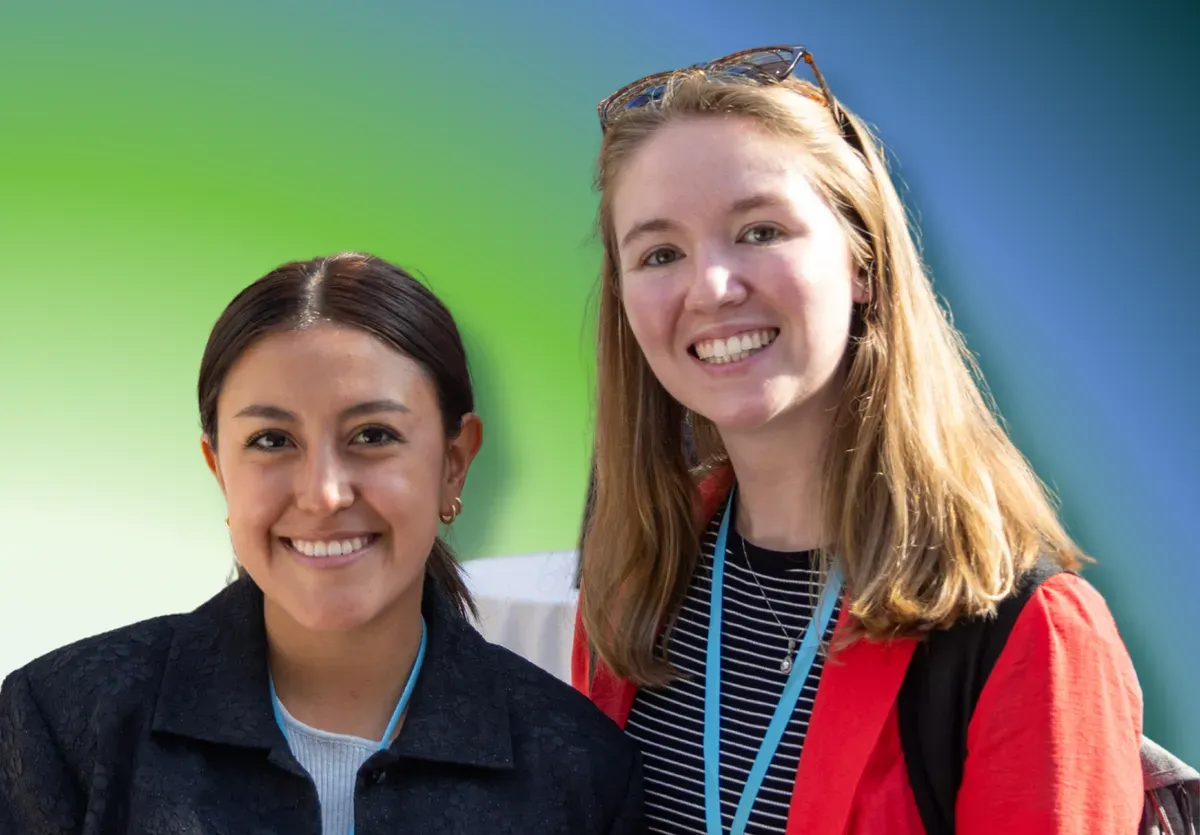 Two people with smiles, one in a dark jacket and the other in a red blazer, against a green and blue background.
