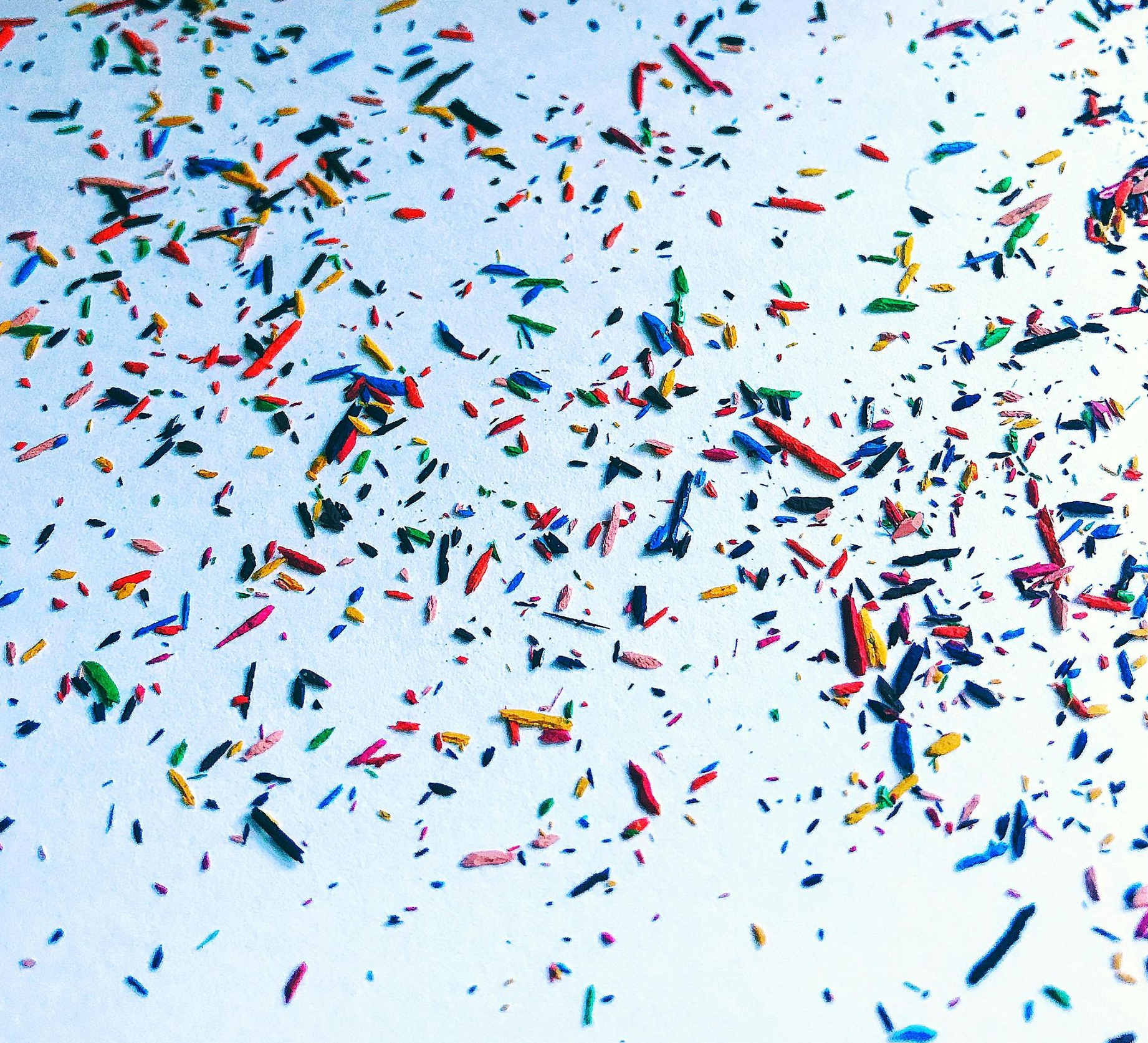 Small, colorful pencil shavings scattered across a white surface.