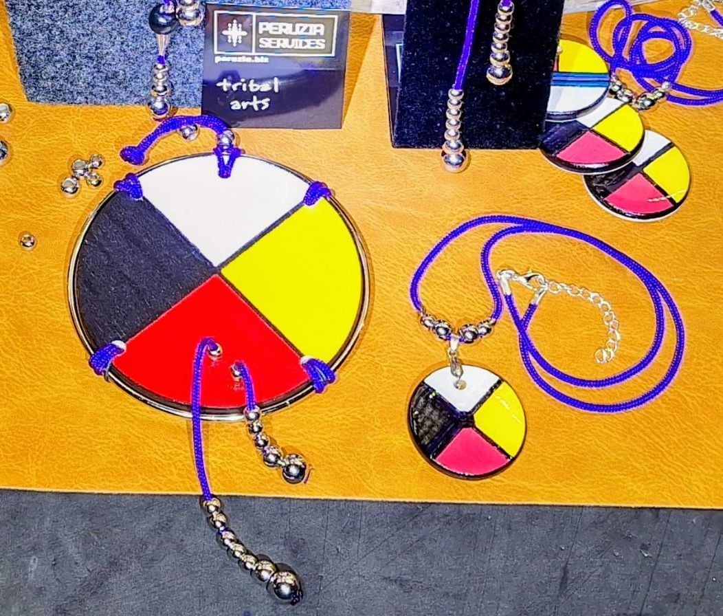 Native American pendants with a four-color wheel design, blue string, and beaded accents on a tan surface.