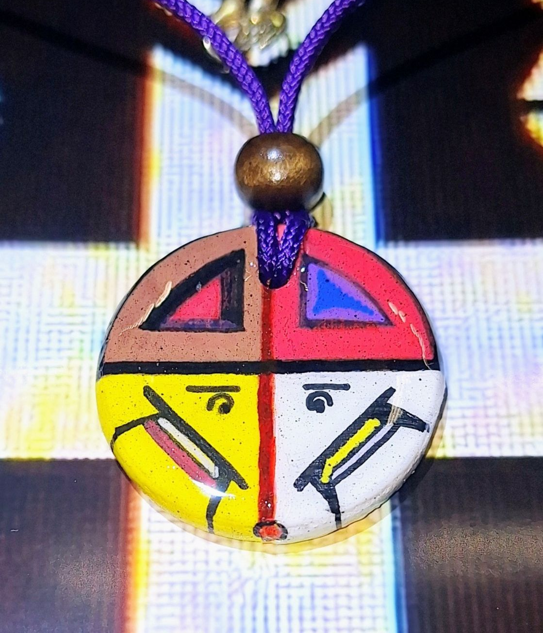 Colorful circular pendant, divided into four sections with symbols and Tibetan script.