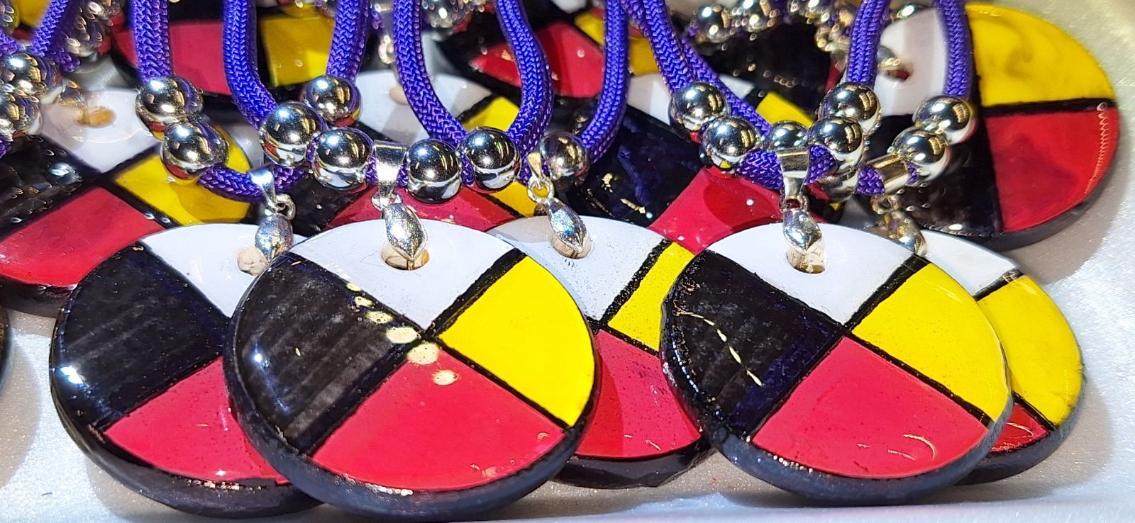 A circular pendant with quadrants of black, white, red, and yellow, on a purple beaded necklace.