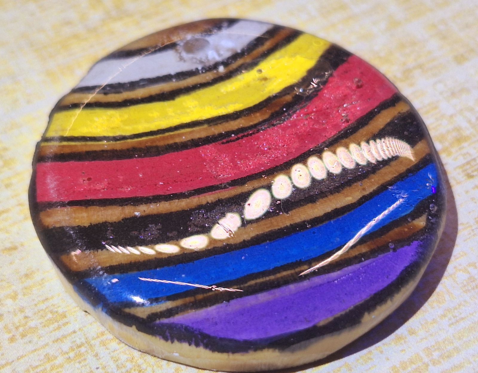 Close-up of a person wearing a necklace with a round pendant. The pendant has colorful stripes, and a brown cord.