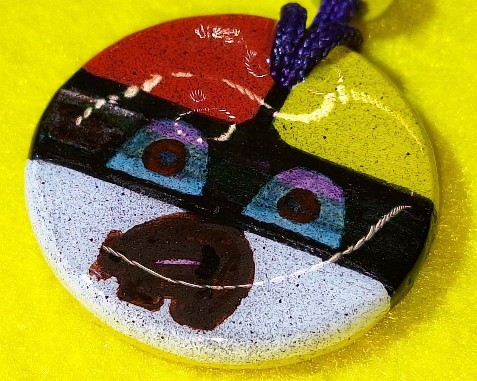 Colorful circular pendant with abstract face design; red, yellow, black, and white sections.